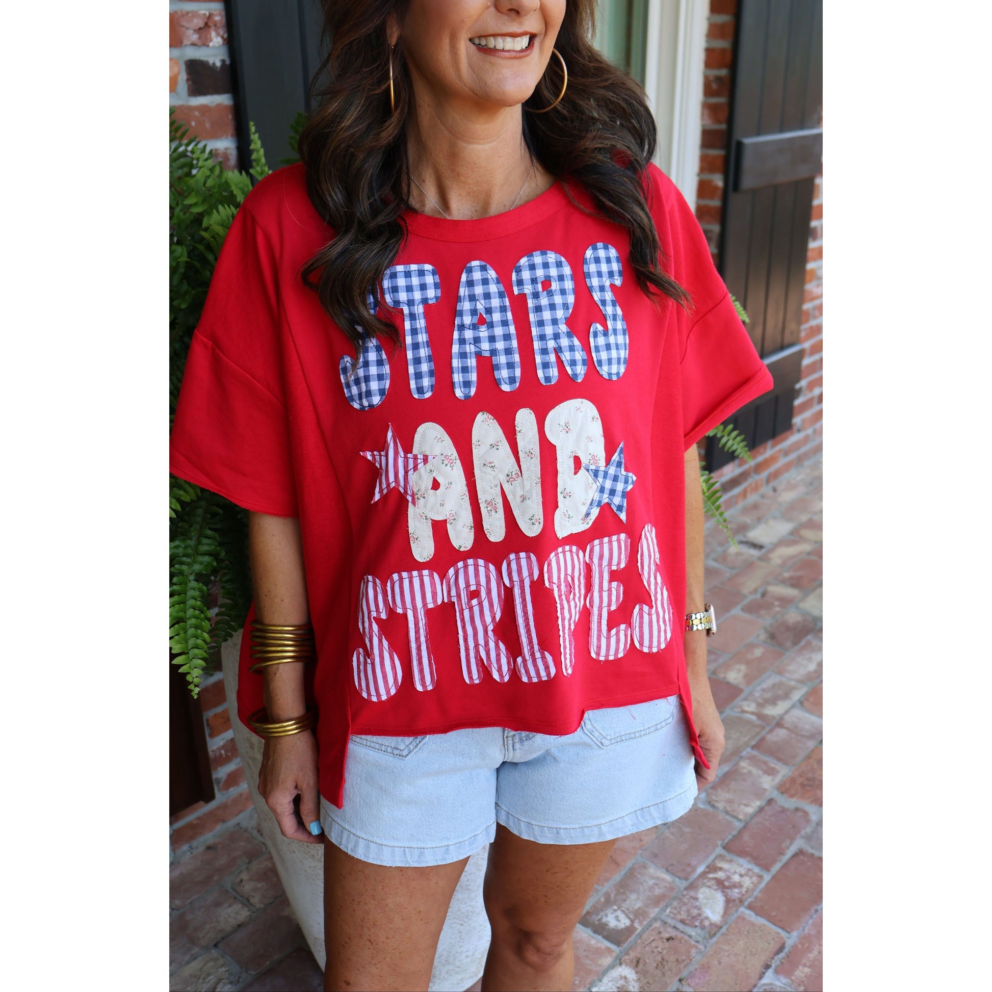 Woman wearing a red t-shirt with 'STARS AND STRIPES' text, standing outdoors.