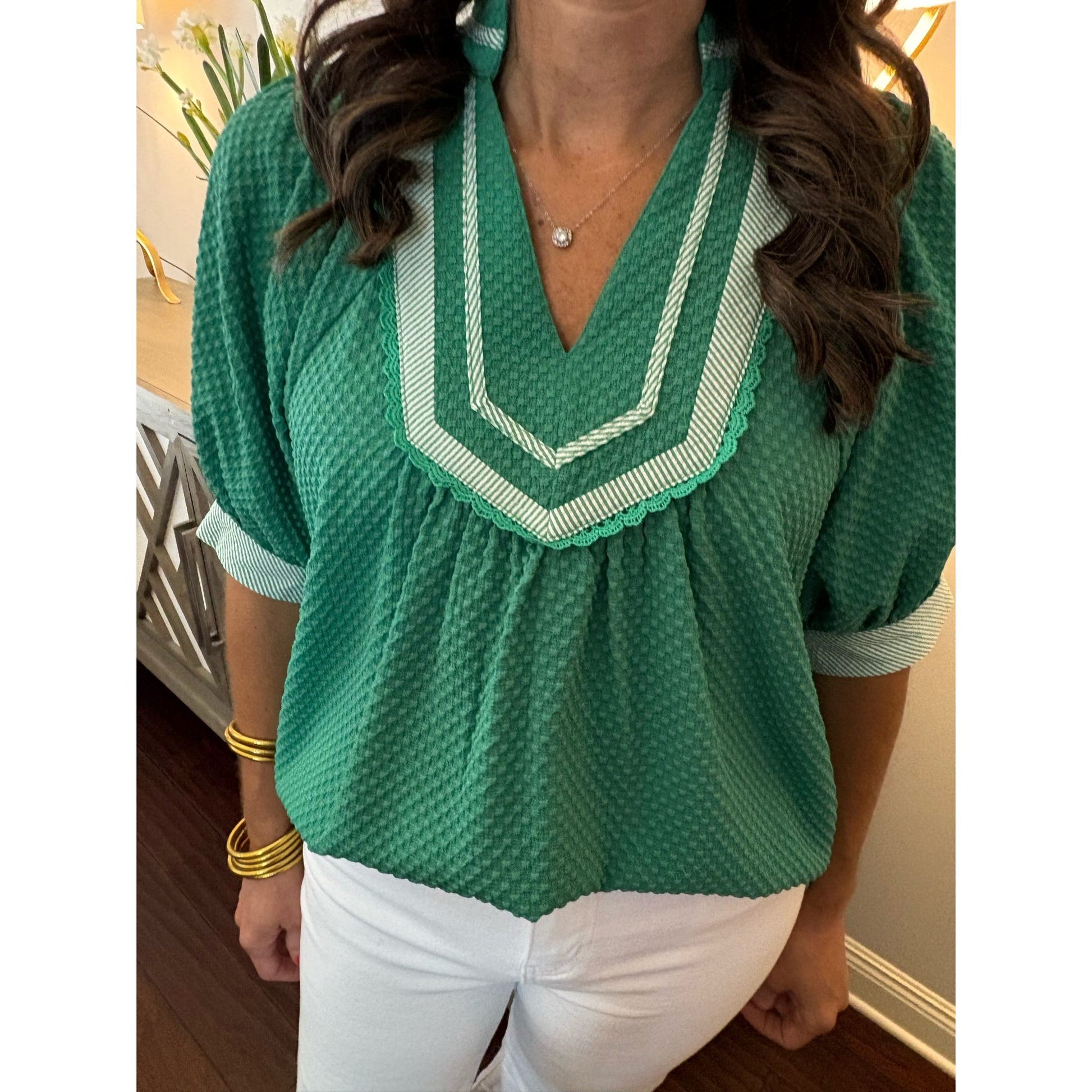 Green blouse with white trim worn by a person indoors