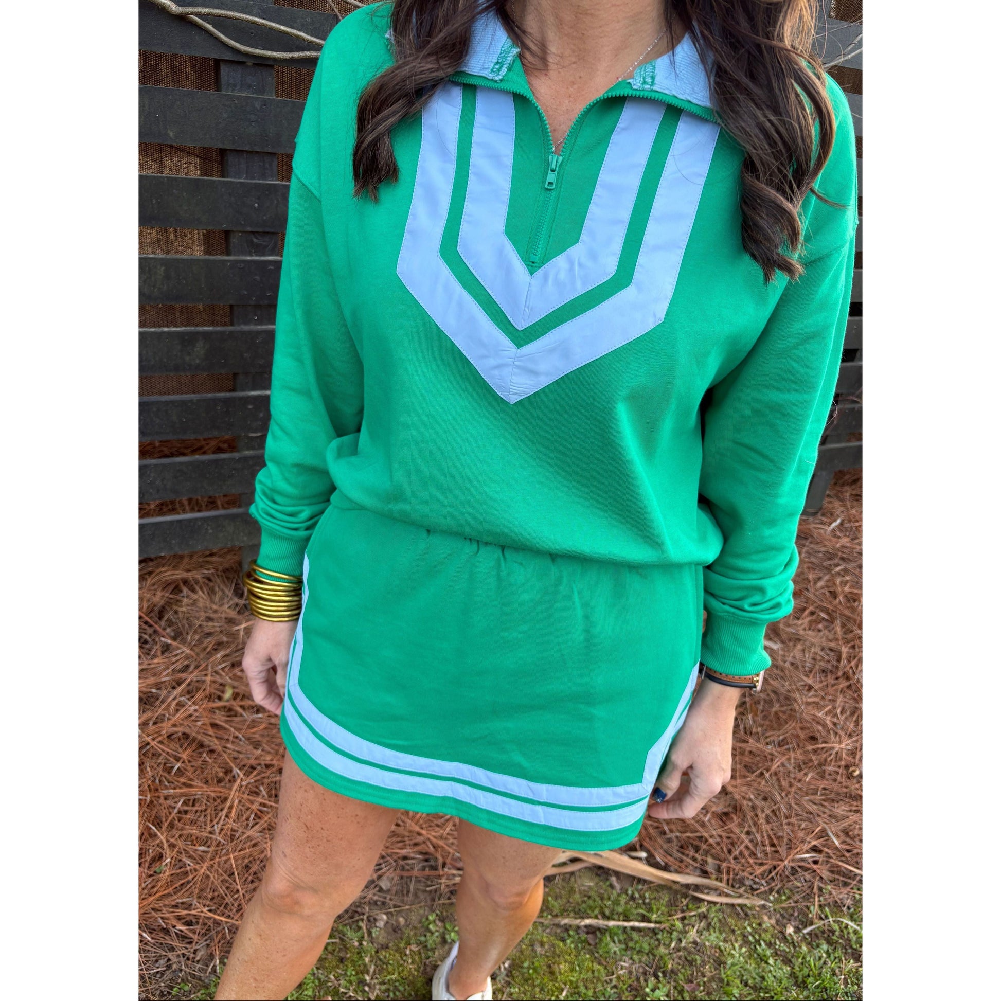 Person wearing a green hoodie with a white logo, standing outdoors on a bench.