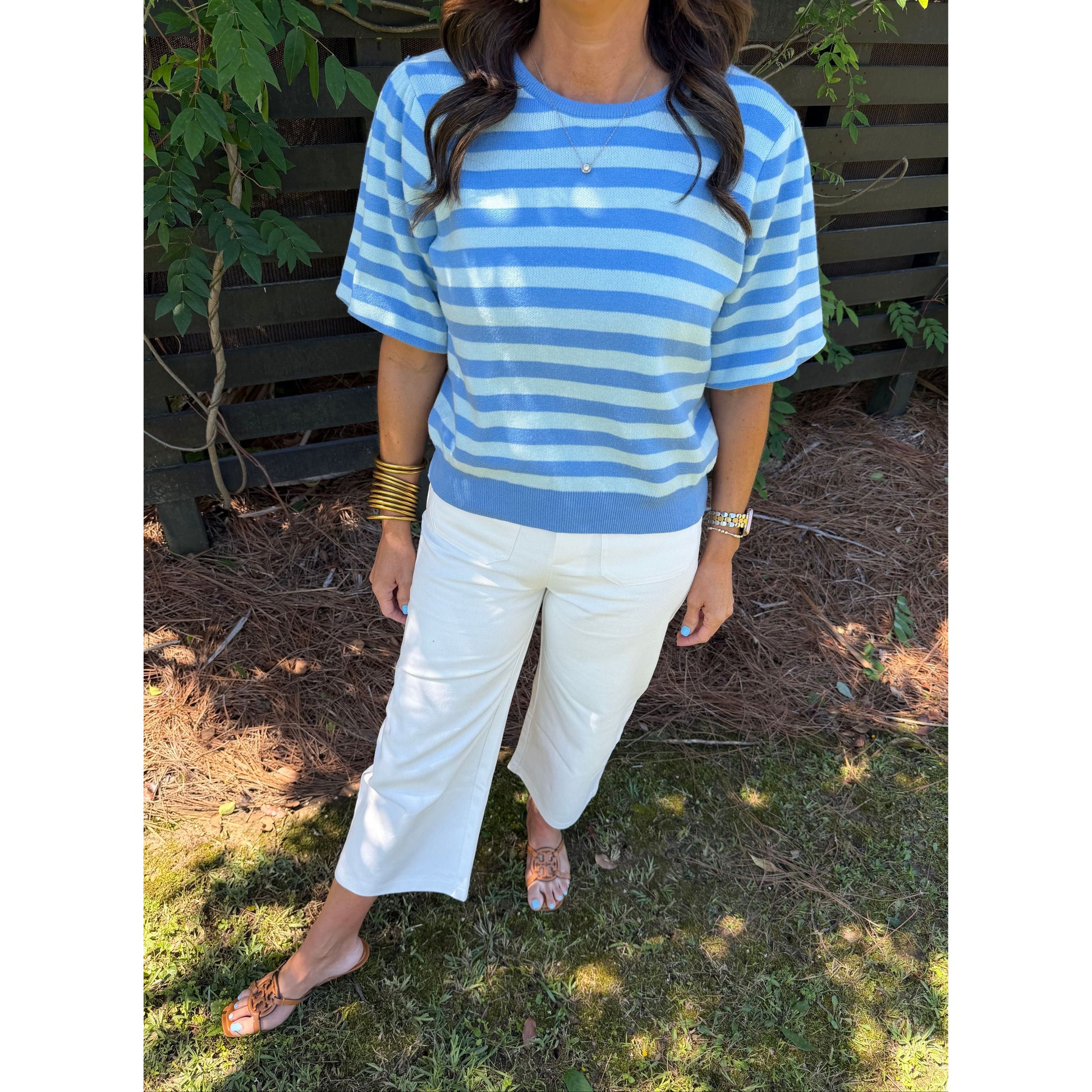 Person wearing a blue and white striped shirt and white pants standing outdoors.