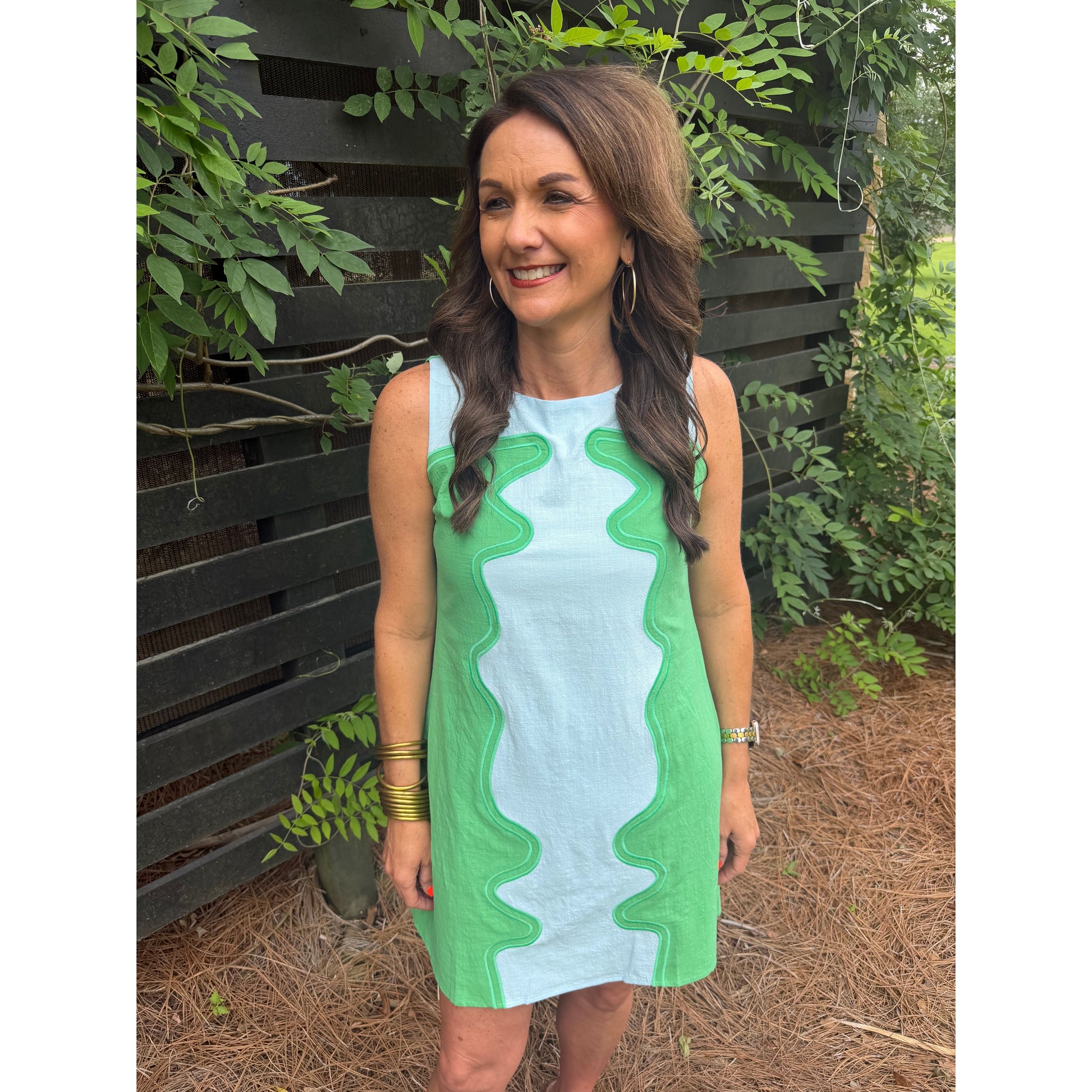 Woman wearing a green and white dress standing outdoors with greenery in the background