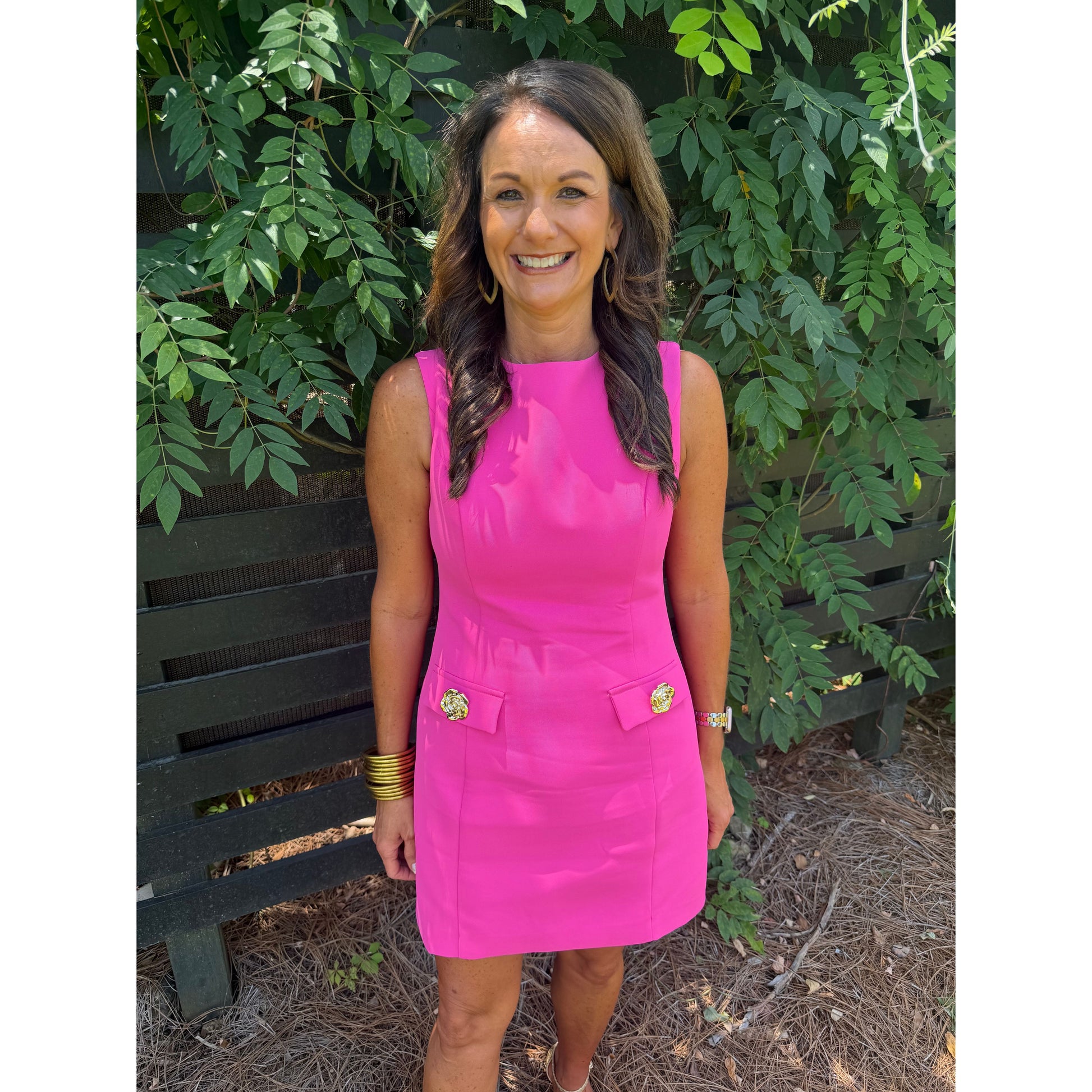 Woman in a pink dress standing outdoors with greenery in the background