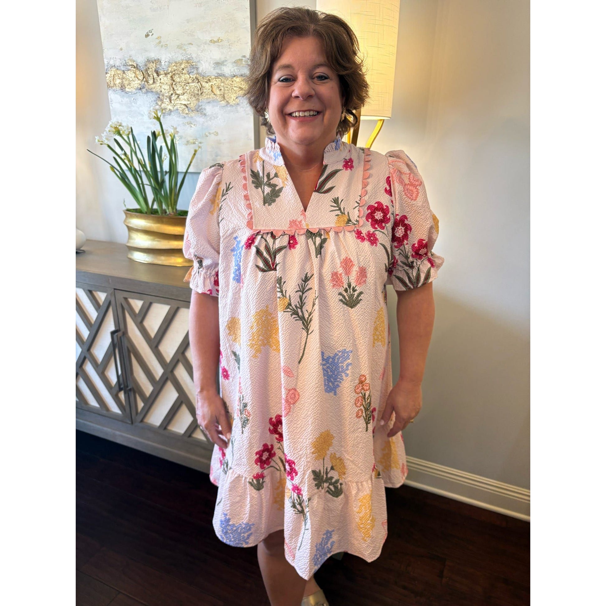 Woman wearing a floral dress in a room with a lamp and plant.