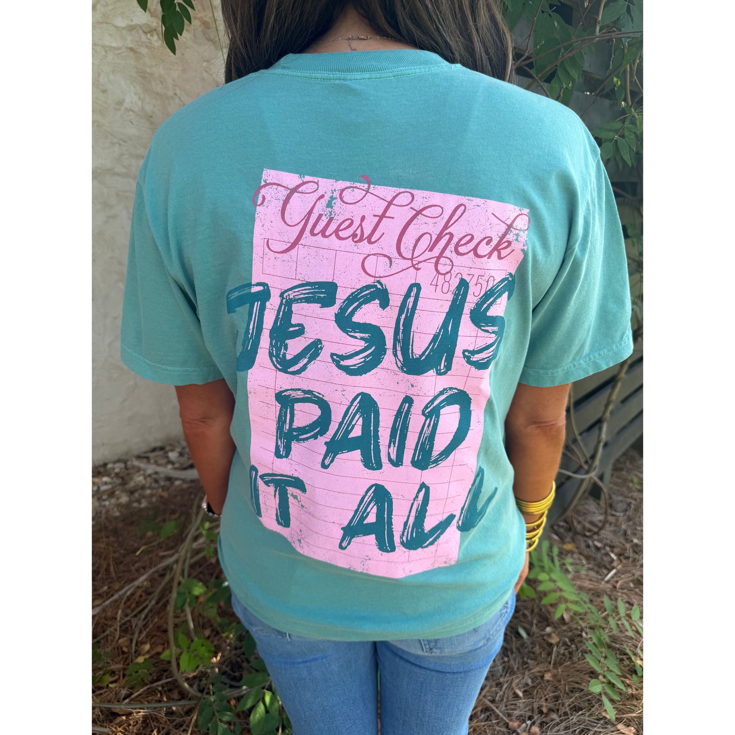 Person wearing a teal t-shirt with a pink and blue graphic on the back, standing outdoors.