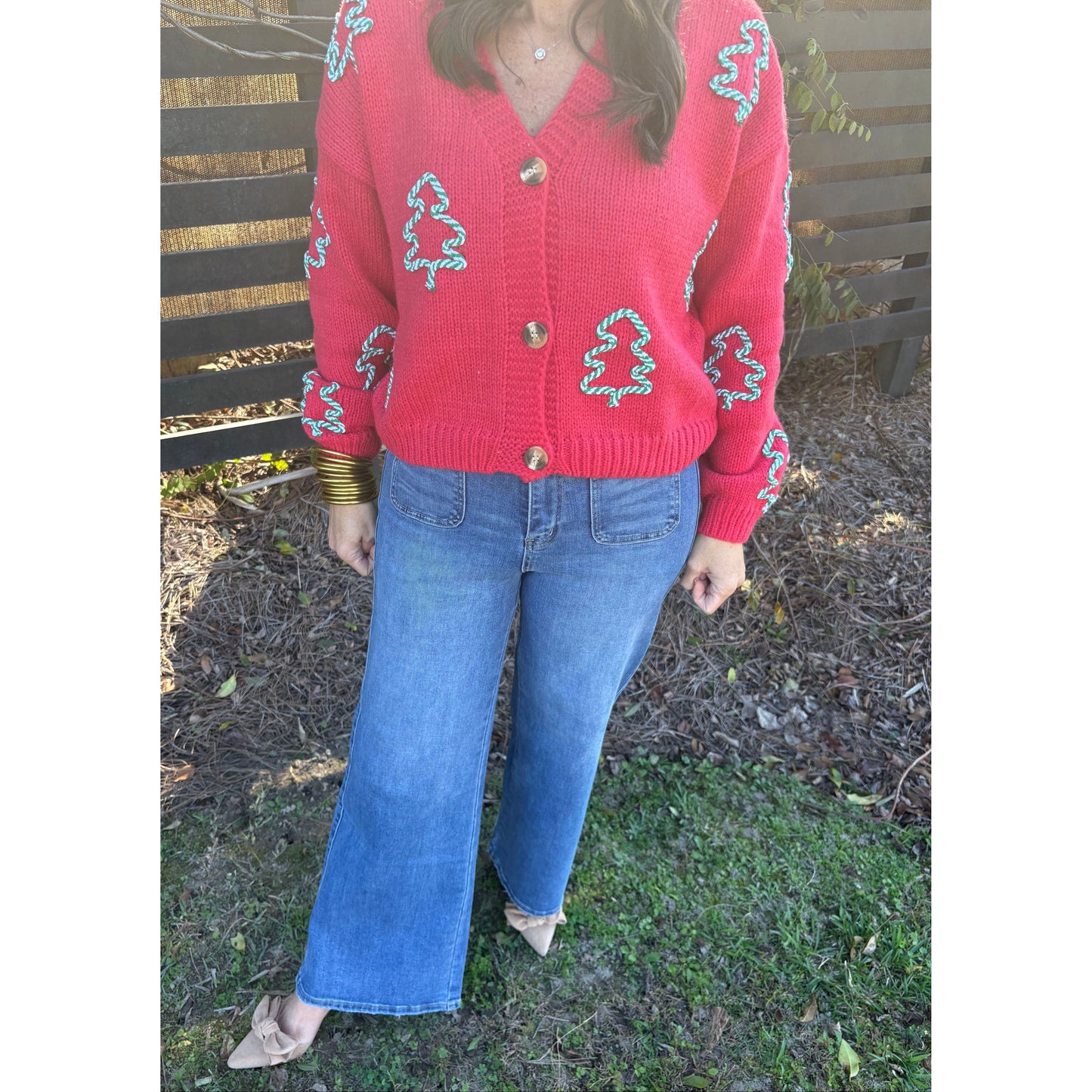 Person wearing a red sweater with white patterns and blue jeans sitting on a wooden bench outdoors.