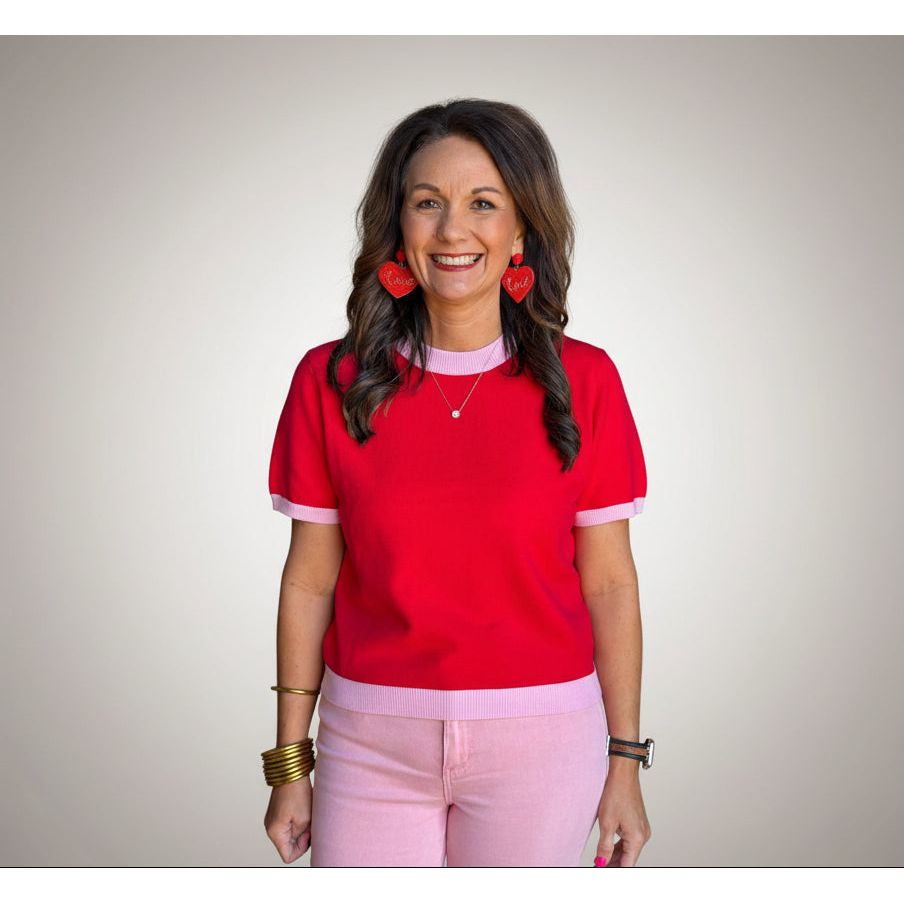 Woman wearing a red sweater with pink trim and pink pants.