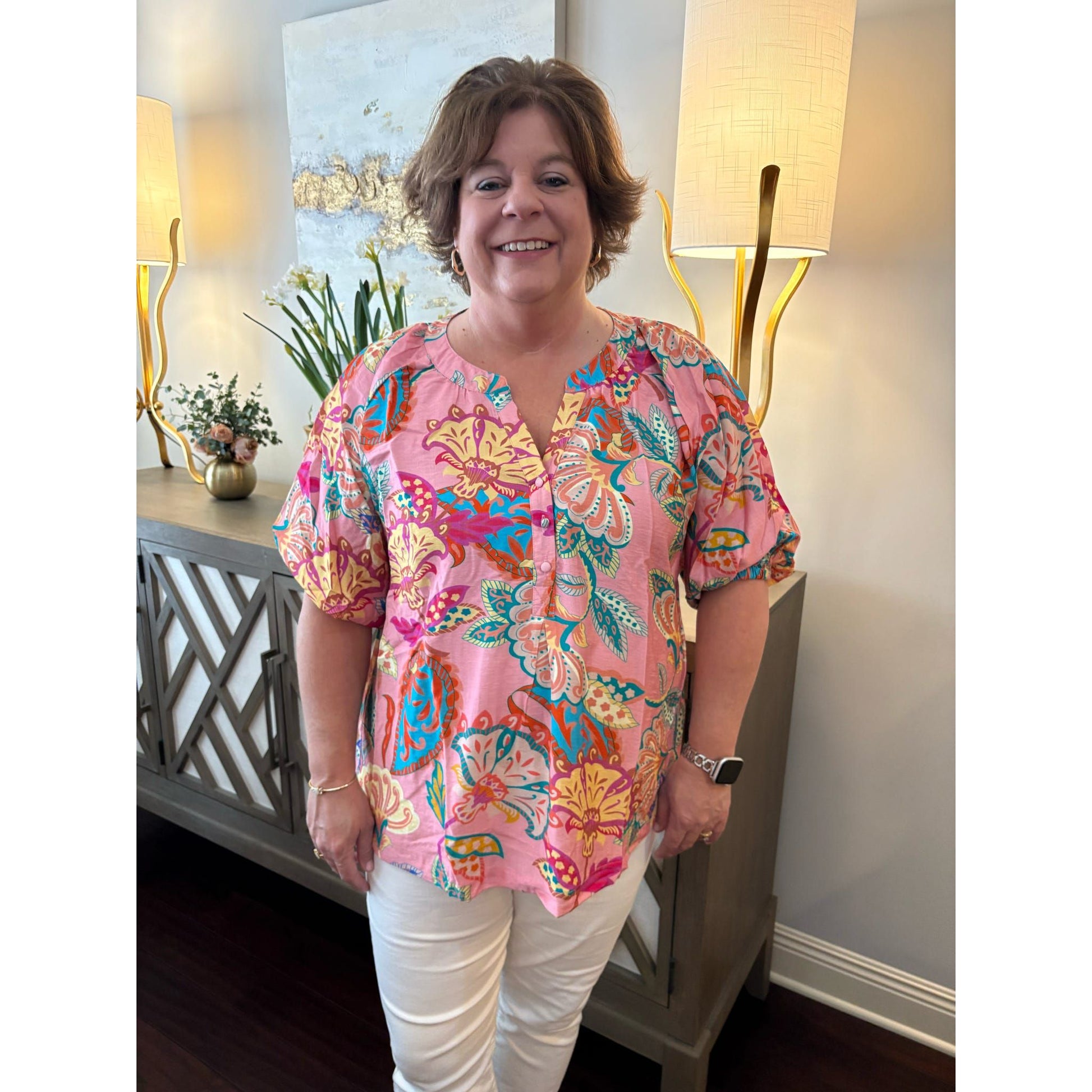 Woman wearing a colorful floral blouse standing in a room with lamps and decor.