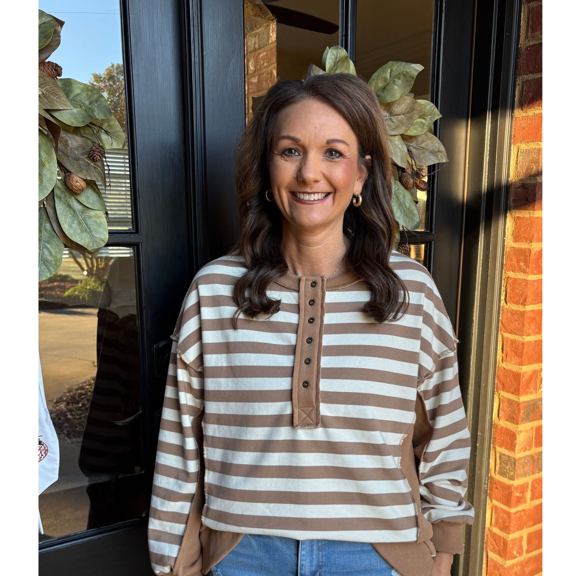 Woman wearing a striped sweater and jeans sitting on a bench with a brick wall background