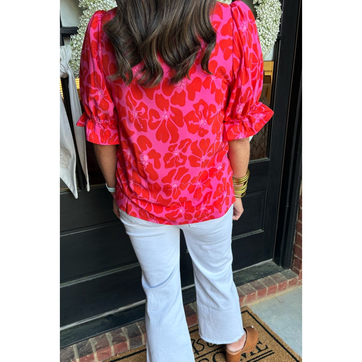 Person wearing a red floral blouse and white pants standing on a doormat with a welcome mat.