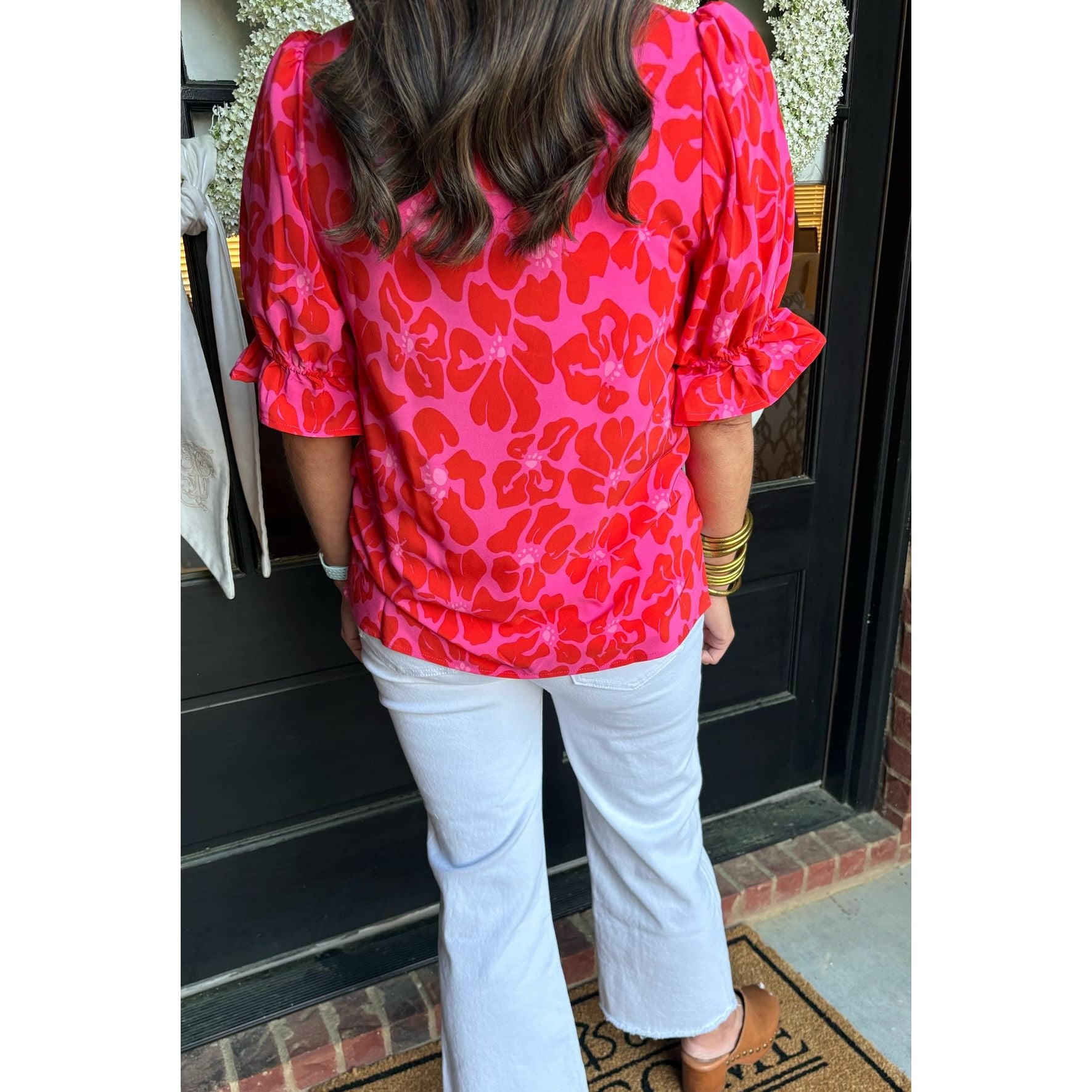 Person wearing a red floral blouse and white pants standing on a doormat with a welcome mat.