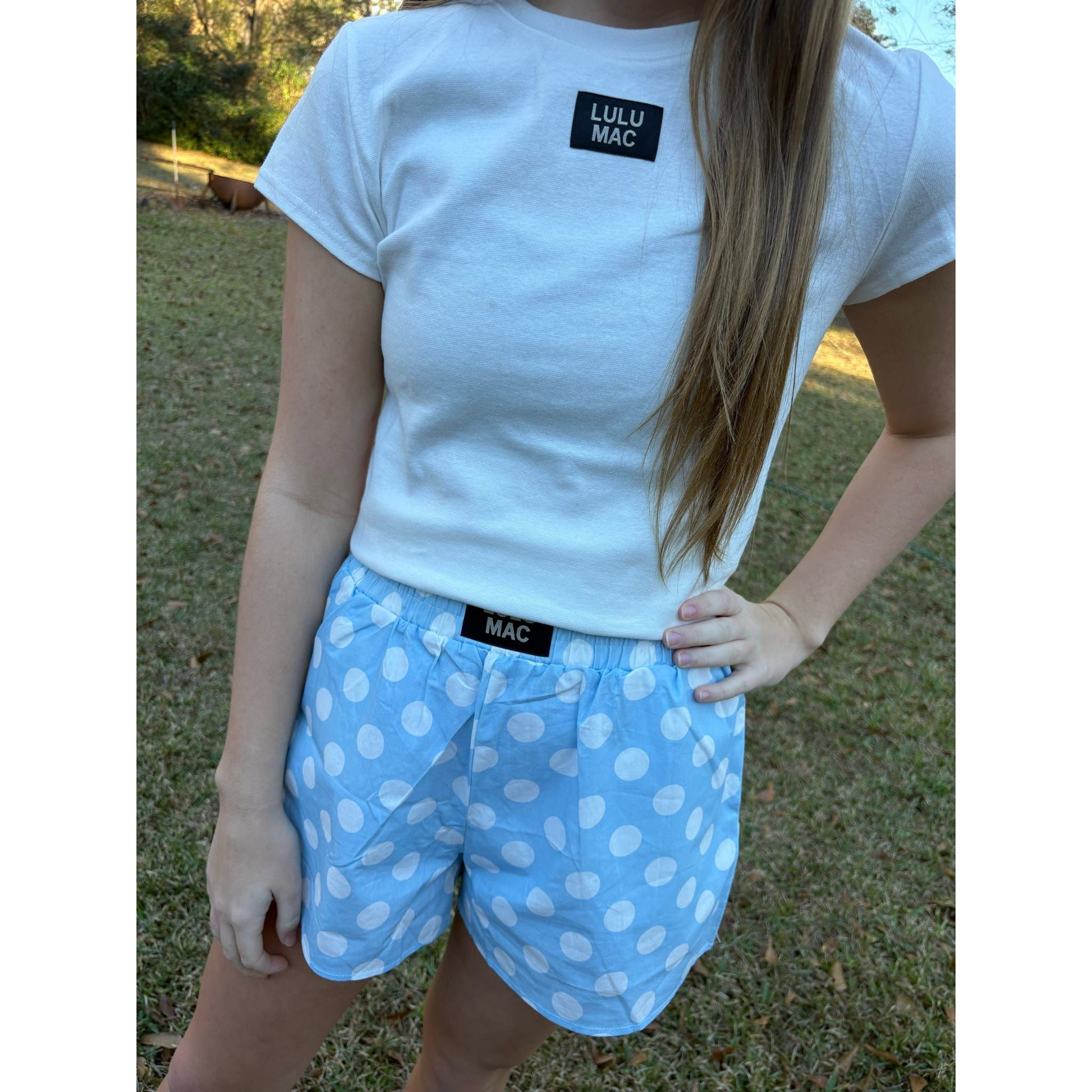 Person wearing a white t-shirt with 'Lulu Mac' branding and light blue polka dot shorts.