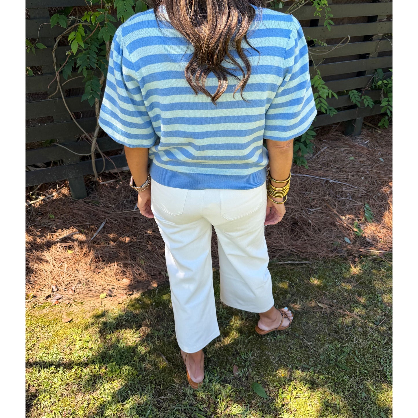 Person wearing a blue and white striped shirt and white pants standing outdoors.