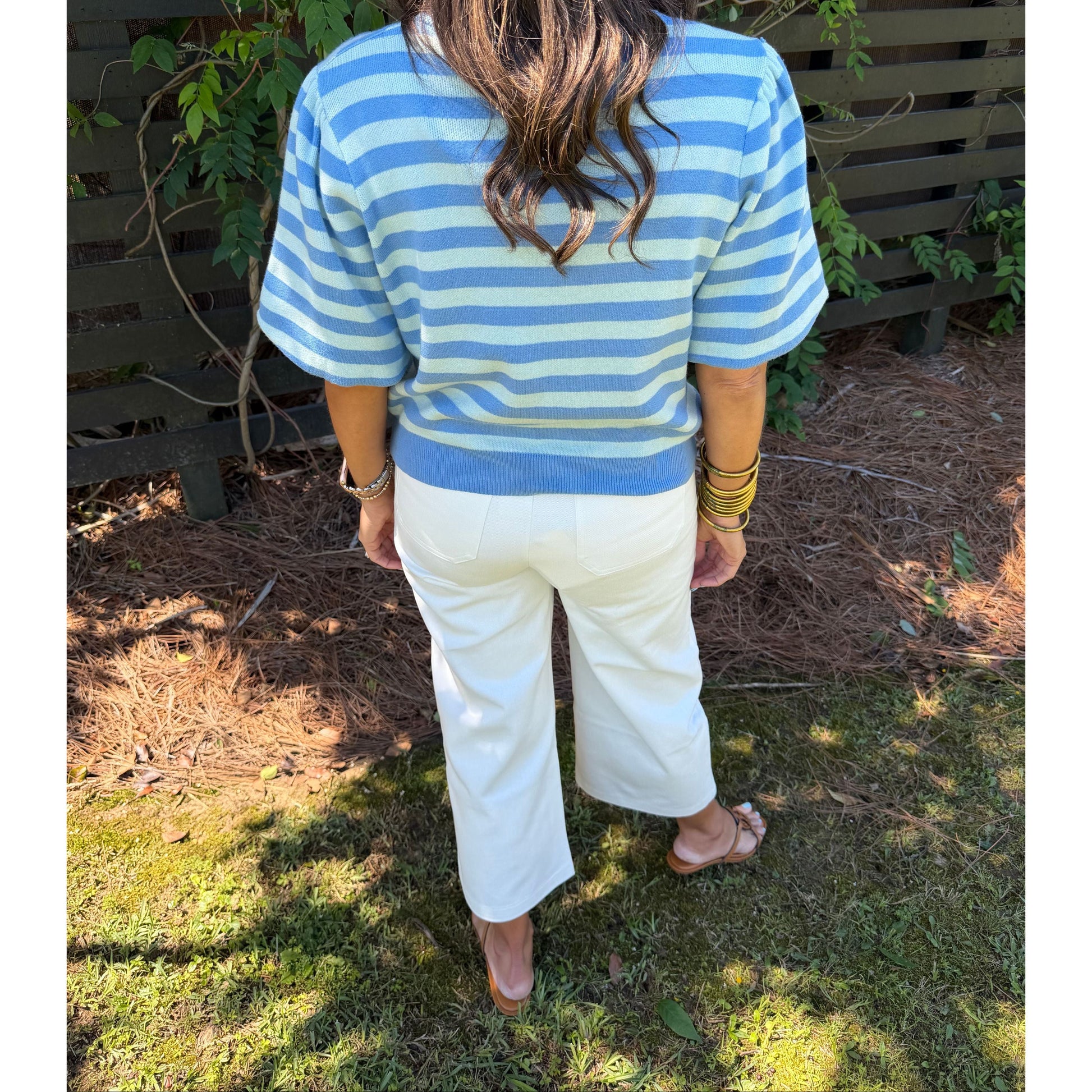 Person wearing a blue and white striped shirt and white pants standing outdoors.