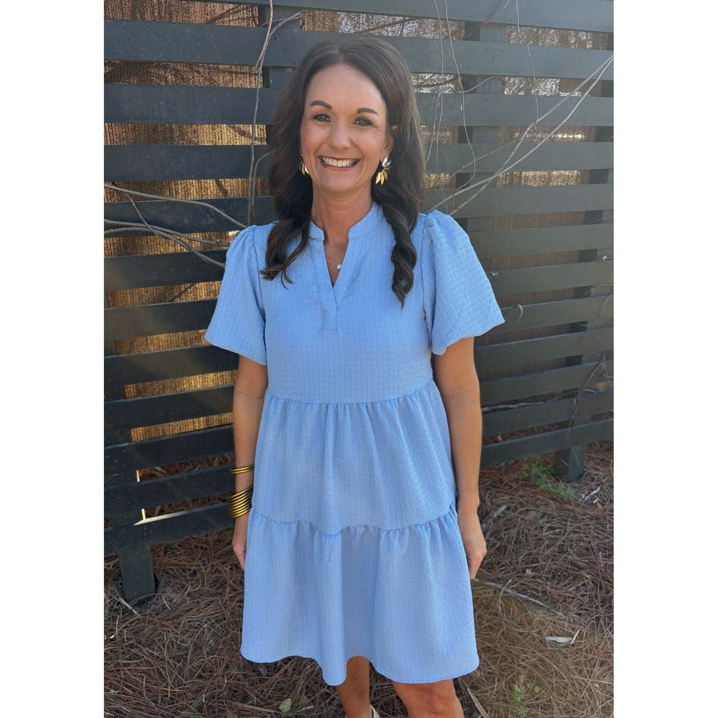 Woman wearing a blue dress standing in front of a wooden fence.