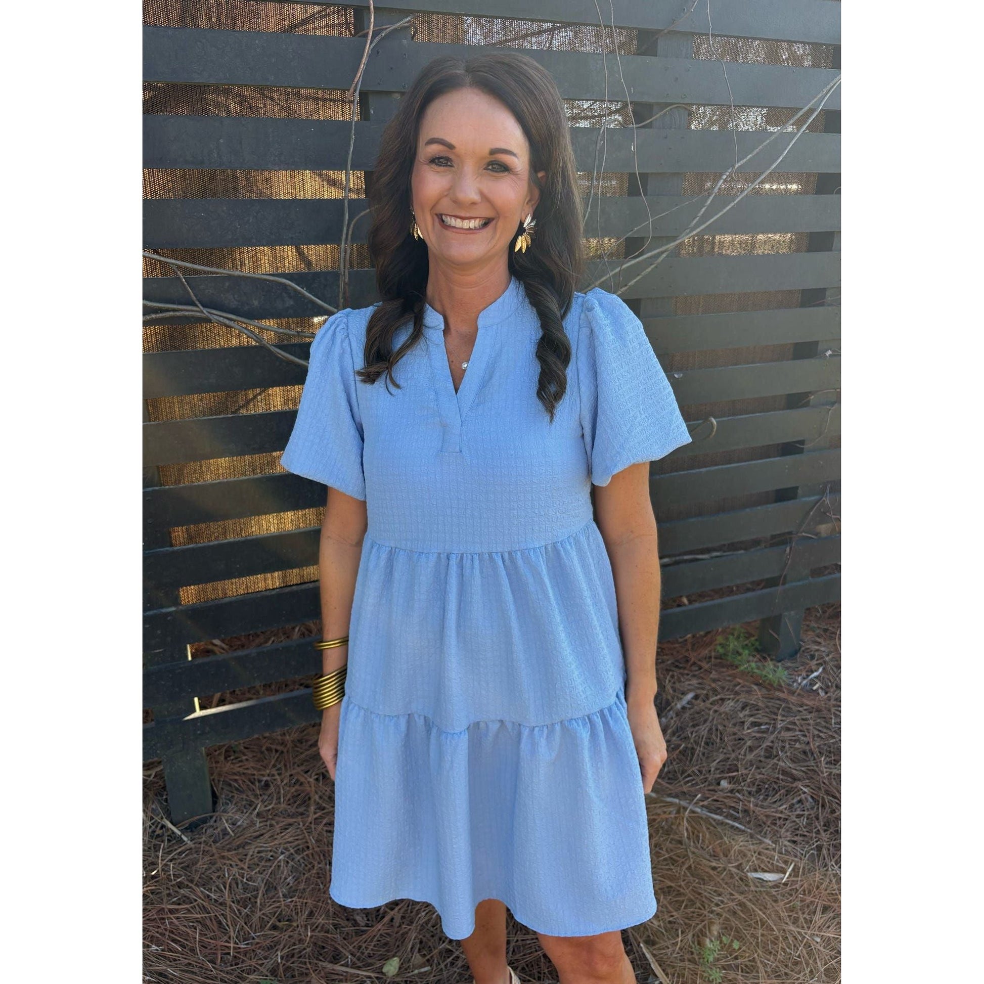 Woman wearing a blue dress standing in front of a wooden fence.