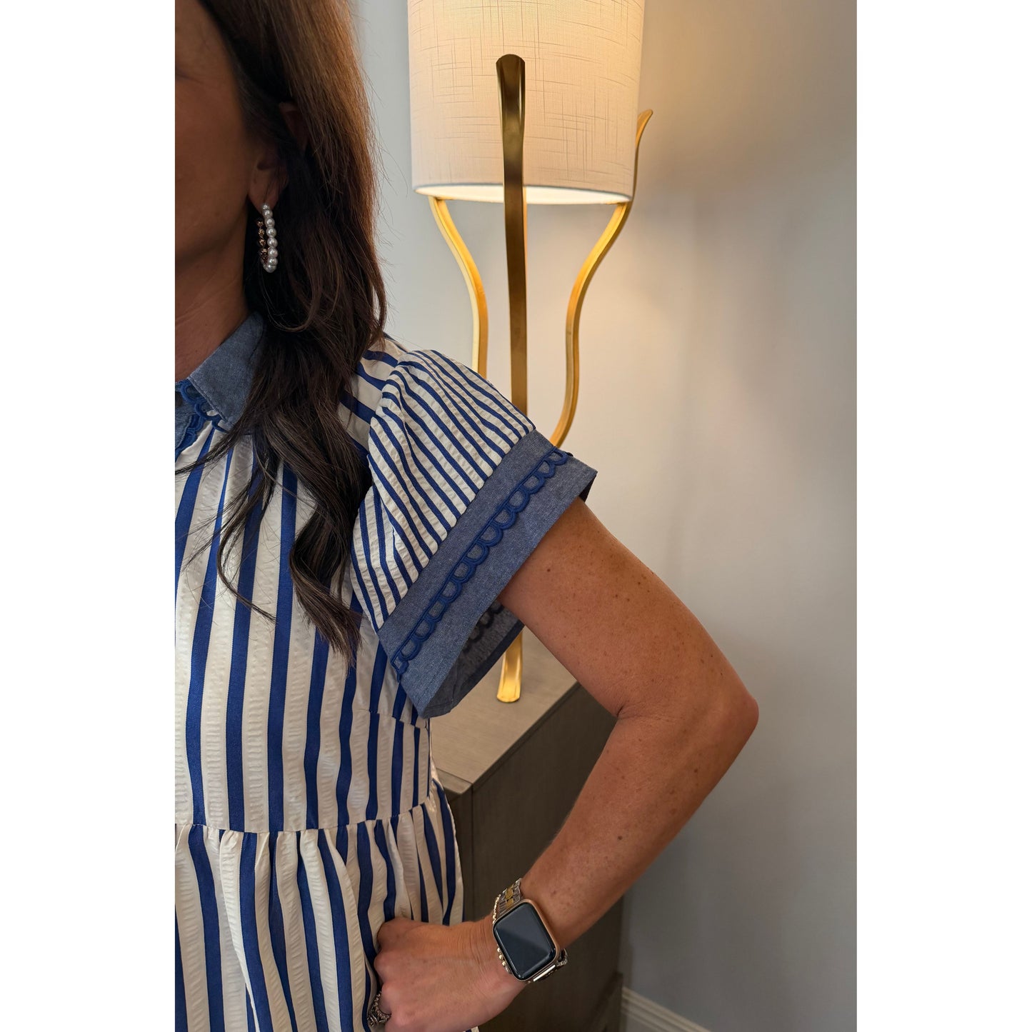 Person wearing a blue and white striped shirt with a lamp and wall in the background
