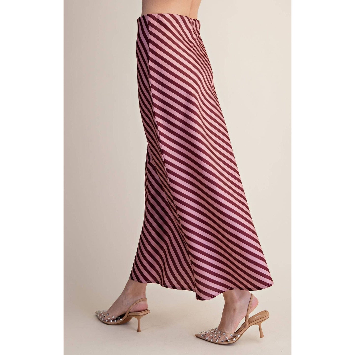 A person wearing a flowing midi skirt with diagonal burgundy and pink stripes, paired with embellished slingback kitten heels, shown against a plain beige studio background.