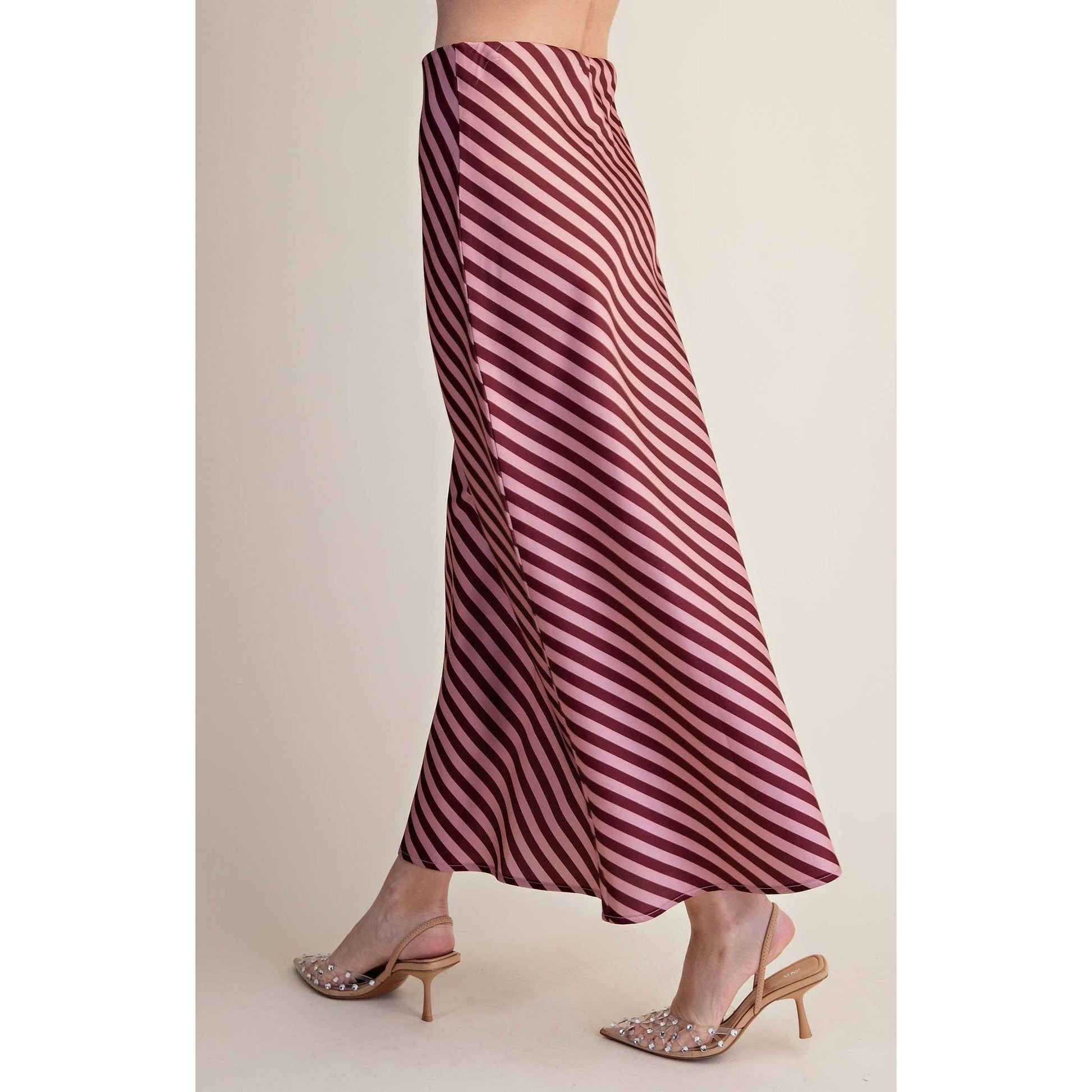 A person wearing a flowing midi skirt with diagonal burgundy and pink stripes, paired with embellished slingback kitten heels, shown against a plain beige studio background.