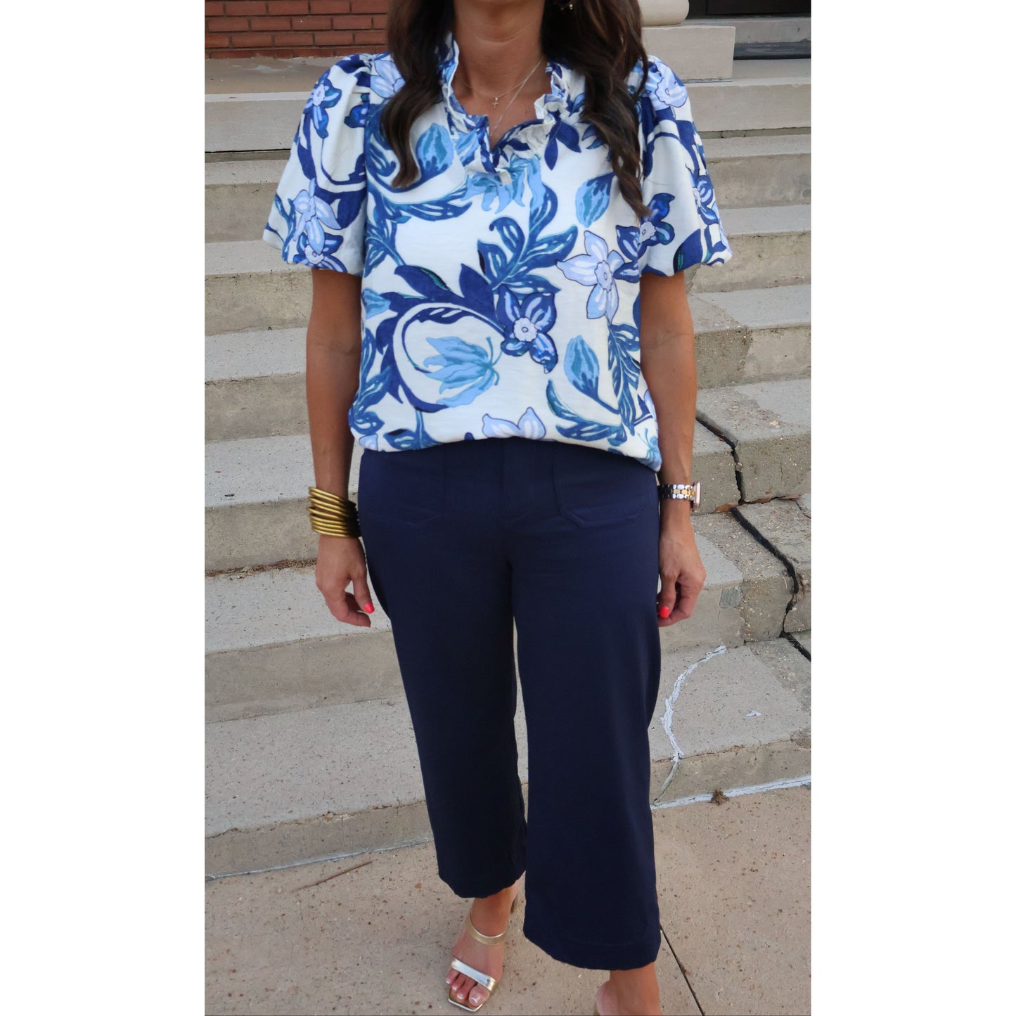 Person wearing a blue and white floral top and dark pants on a concrete staircase.