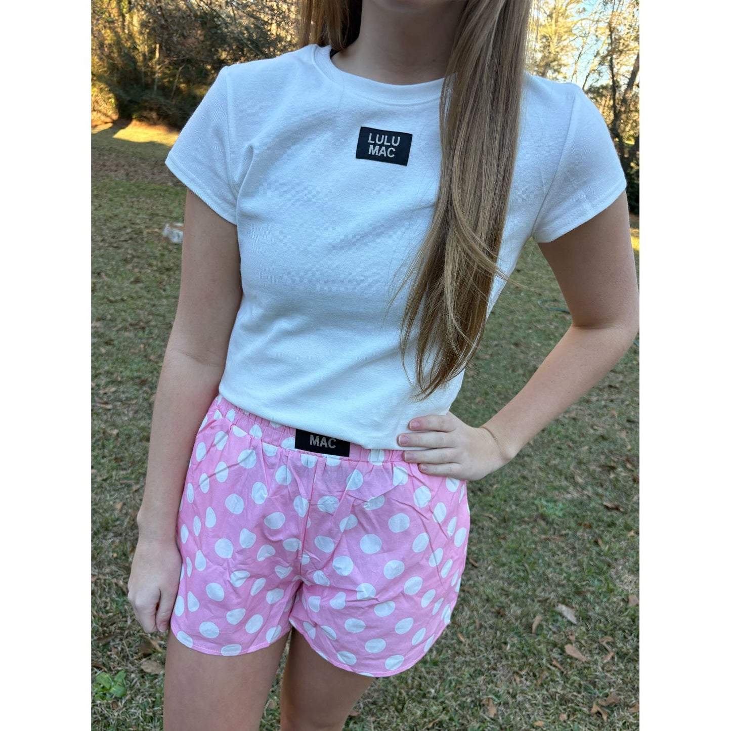 Person wearing a white t-shirt and pink polka dot shorts with 'Lulu Mac' branding outdoors.