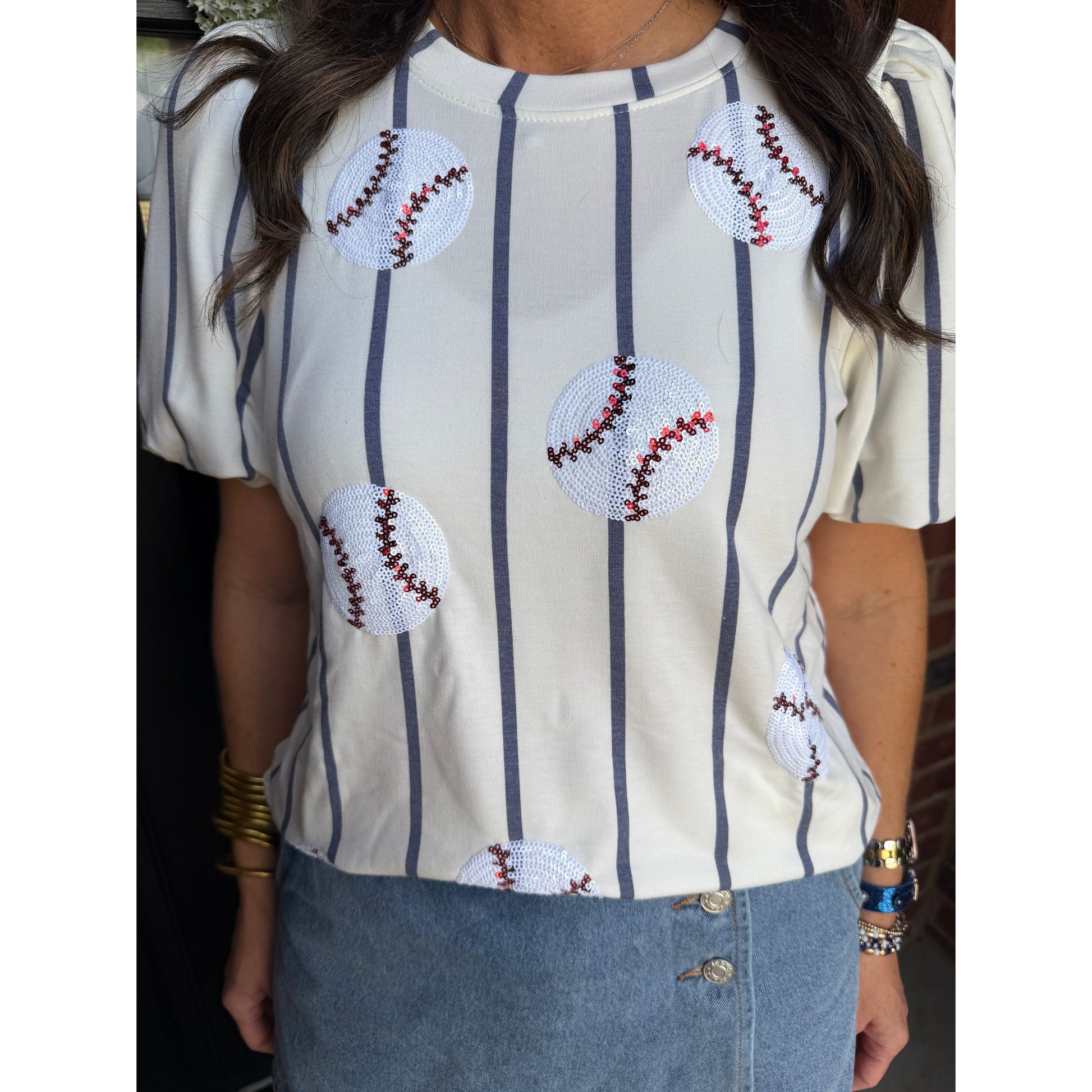 Person wearing a striped shirt with baseball designs and denim pants.