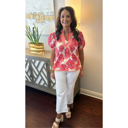 Woman wearing a floral blouse and white pants standing in a room with decorative elements.