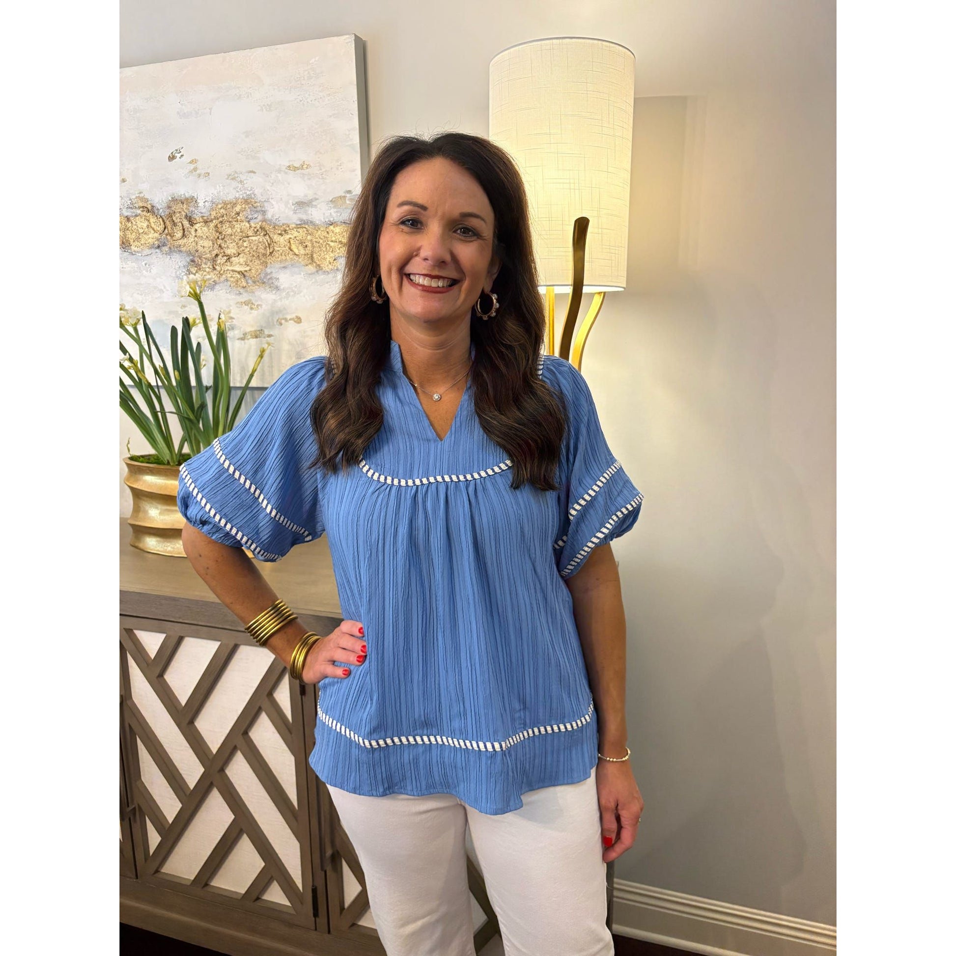 Woman wearing a blue blouse with white trim in an indoor setting.