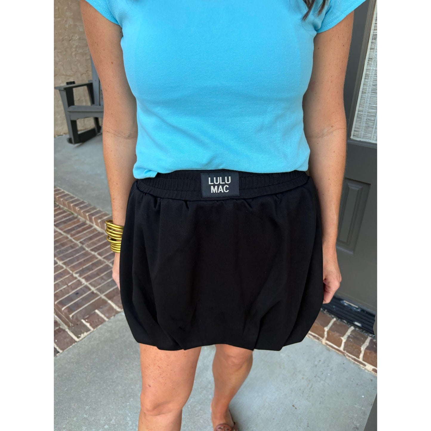 Person wearing a blue shirt and black Lulu Mac shorts on a sidewalk.