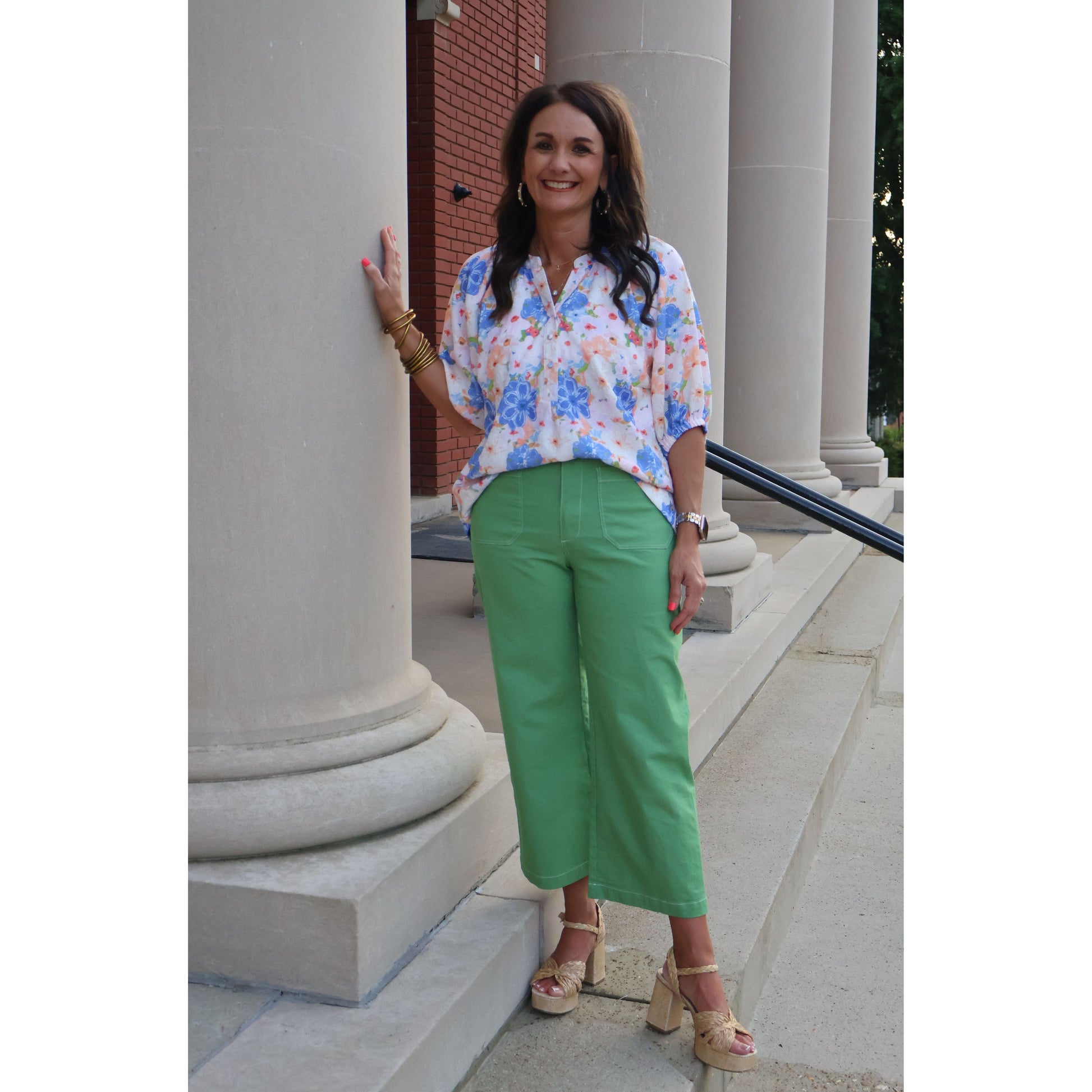 Woman in floral blouse and green pants standing on a stone staircase.
