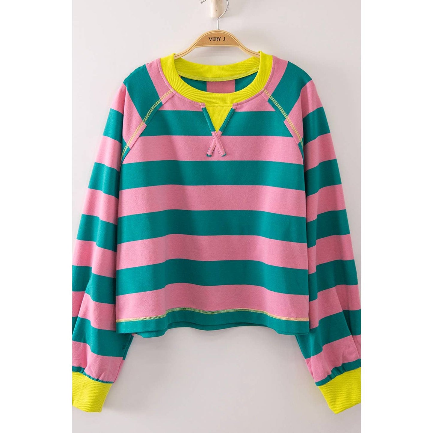 A long-sleeve striped top with horizontal pink and teal stripes, featuring a bright neon yellow collar, hem, and cuffs, hanging on a wooden hanger against a plain light background.