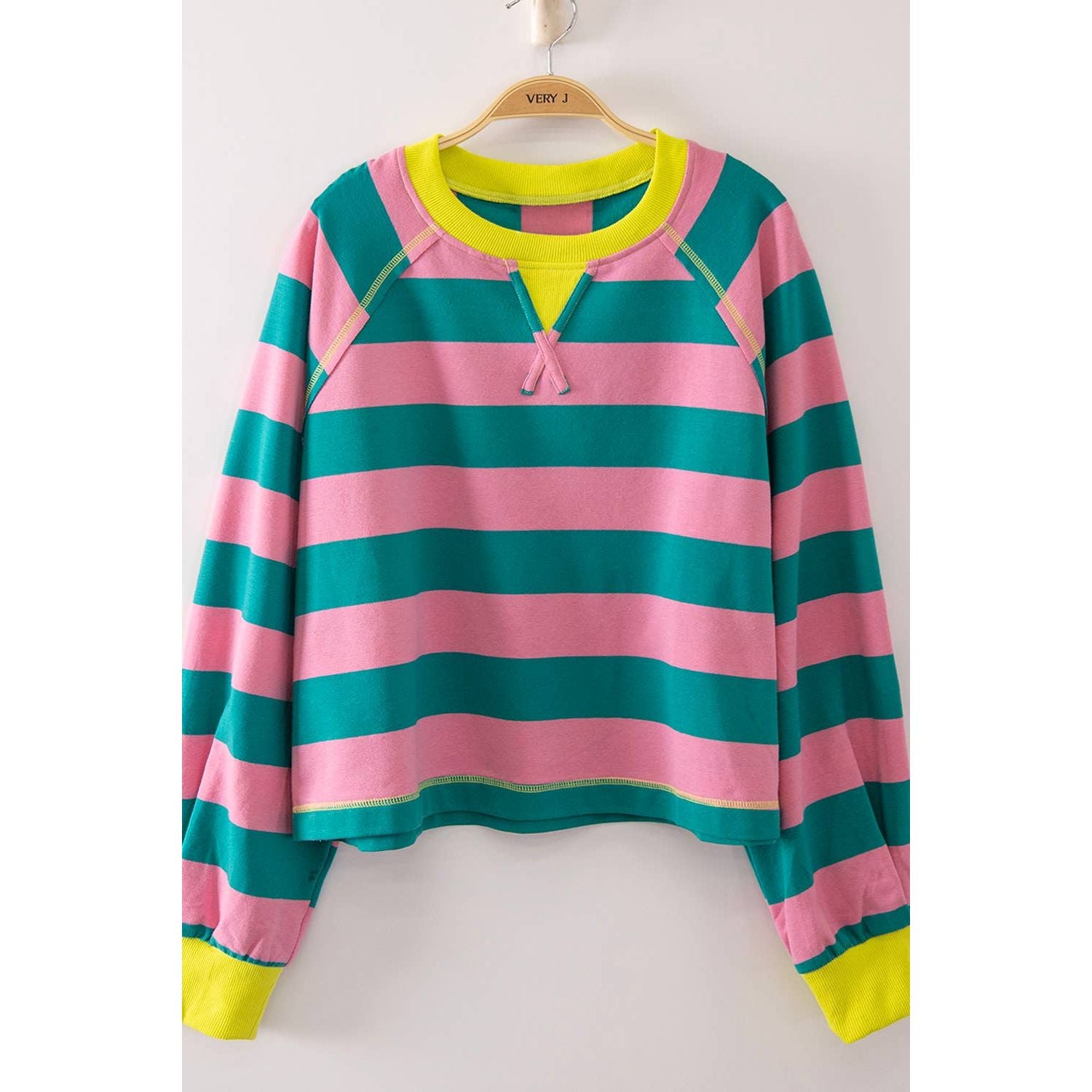A long-sleeve striped top with horizontal pink and teal stripes, featuring a bright neon yellow collar, hem, and cuffs, hanging on a wooden hanger against a plain light background.