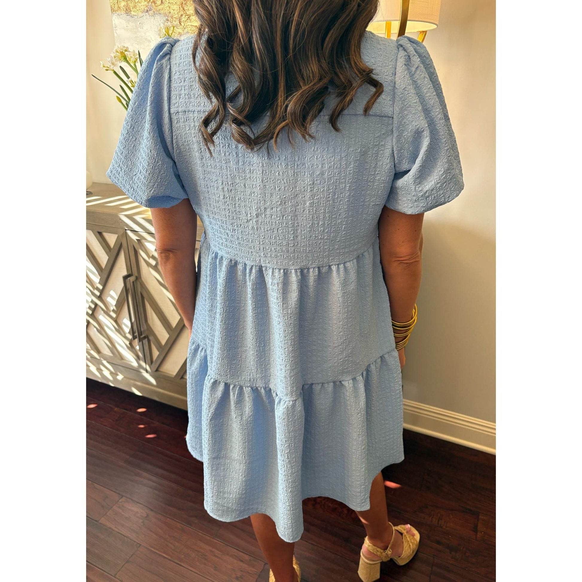 Person wearing a light blue dress with puffed sleeves in an indoor setting.
