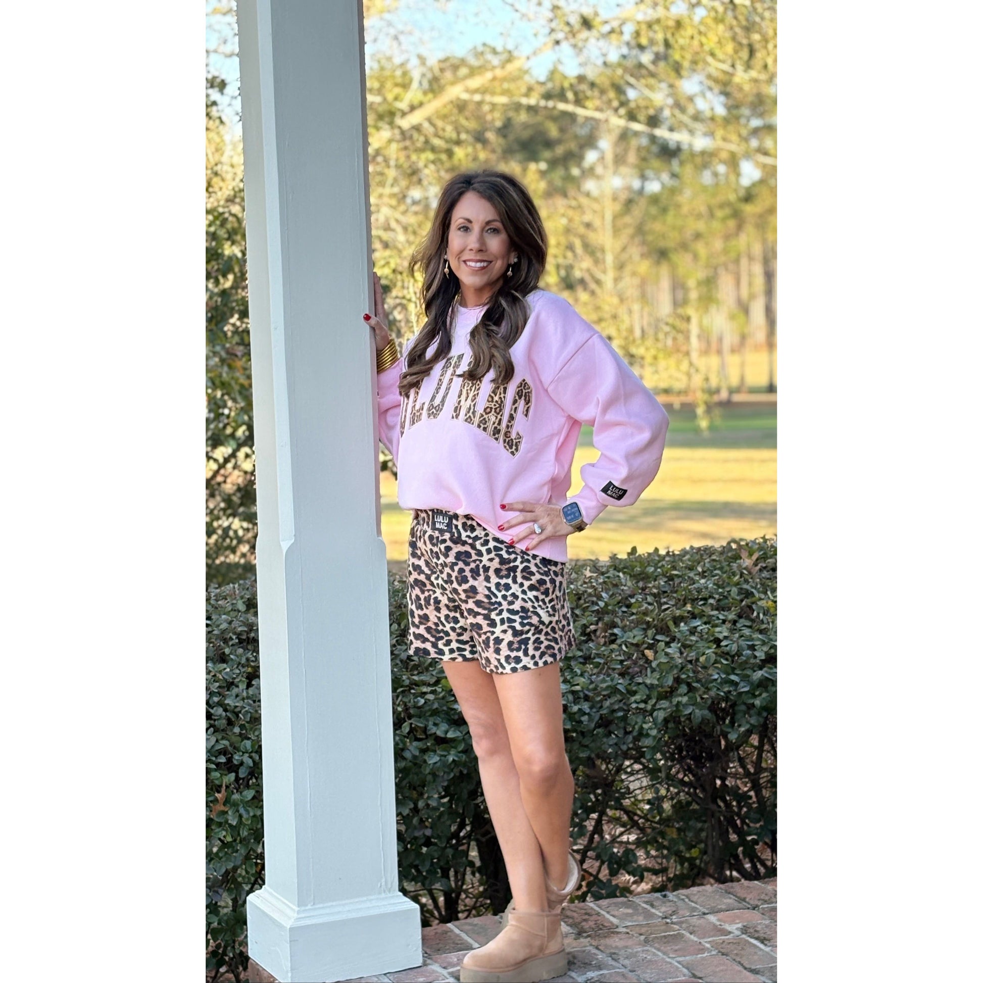 Woman wearing a pink sweatshirt with text and a leopard print skirt outdoors.