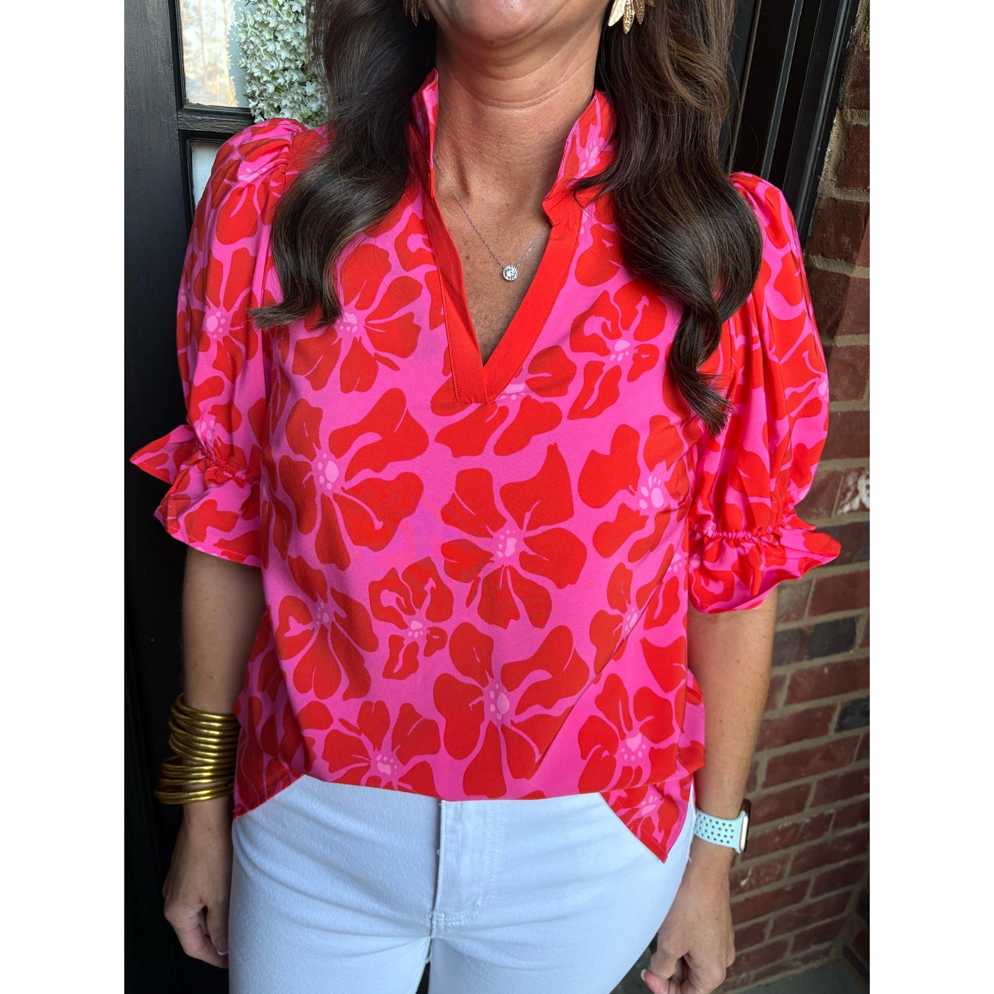 Person wearing a bright pink floral blouse with ruffled sleeves in front of a brick wall.