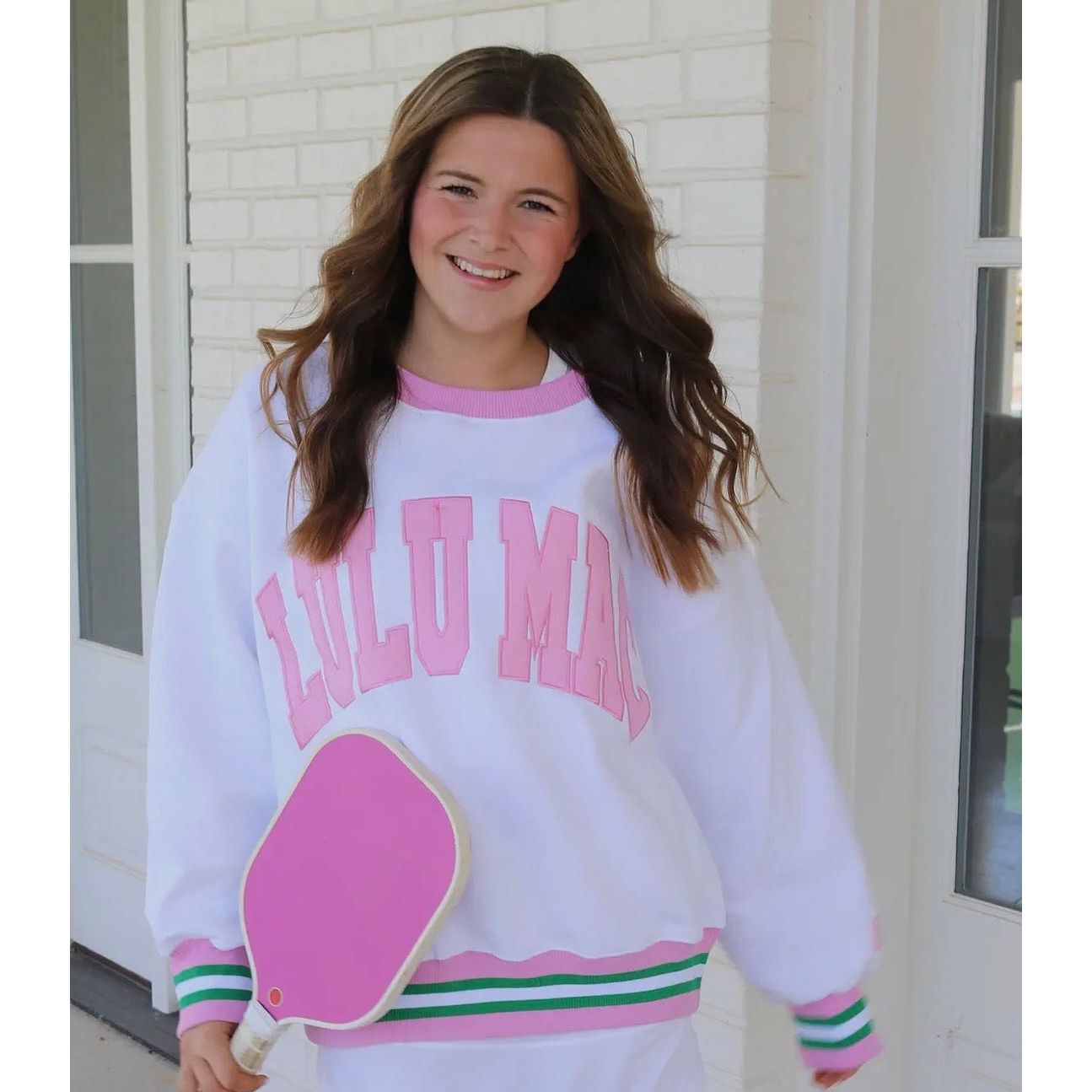Young girl wearing a white sweatshirt with pink text and graphics, standing outside a building.
