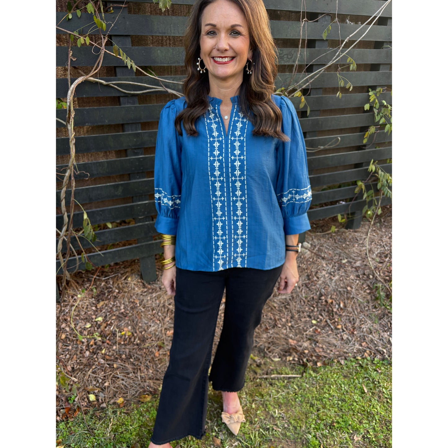 Woman in a blue shirt with white patterns standing outdoors on a bench.