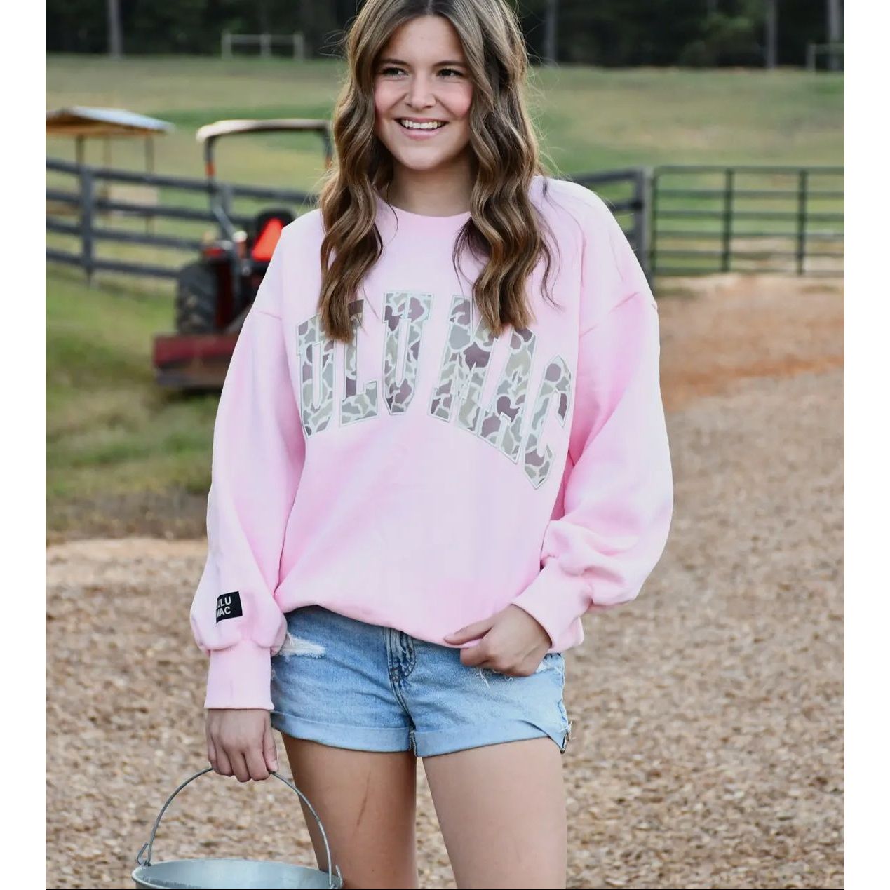 Woman wearing a pink sweatshirt with a graphic design, standing outdoors.