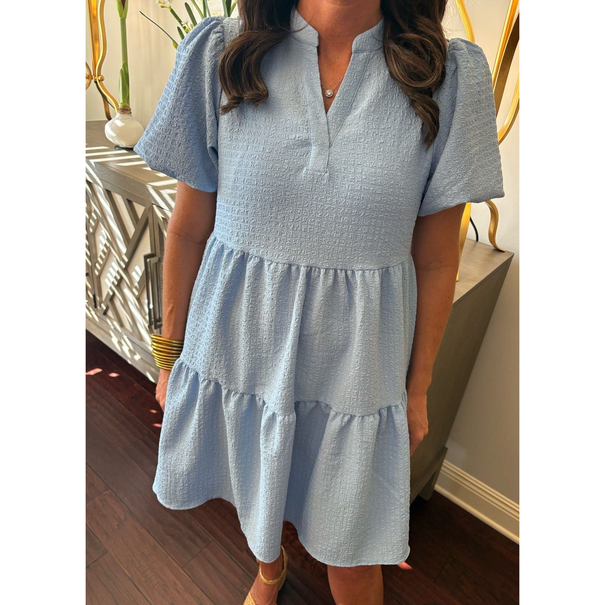 Woman wearing a light blue dress with ruffled sleeves and bottom hem in an indoor setting.