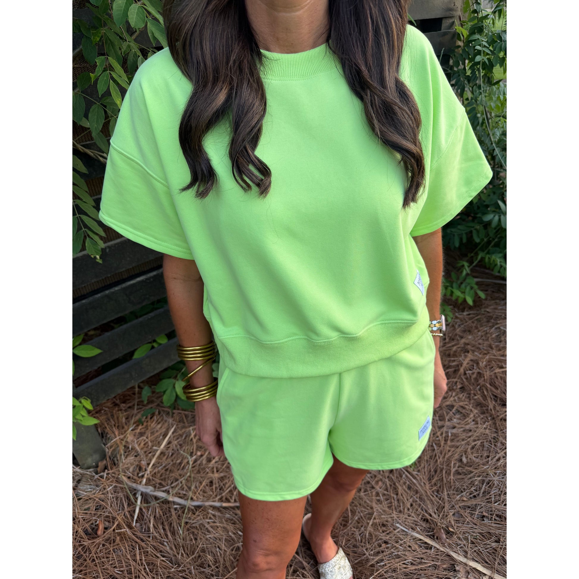 Person wearing a bright green outfit standing outdoors with plants in the background