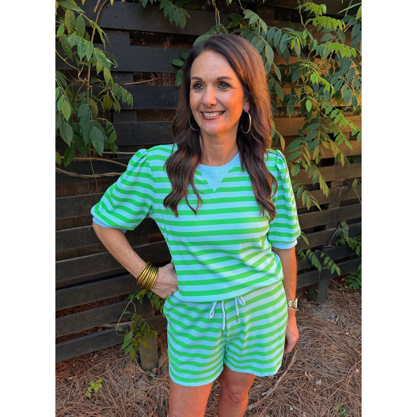 Woman wearing a green and white striped outfit sitting outdoors.