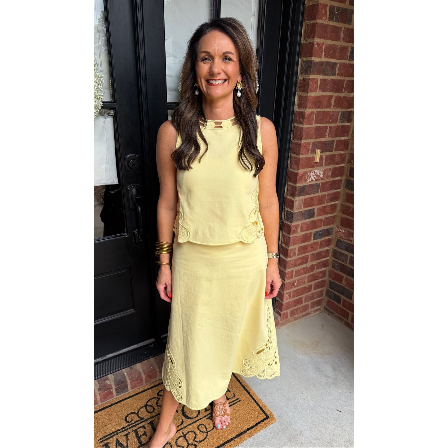 Woman in a yellow dress standing in front of a door with a wreath and doormat.