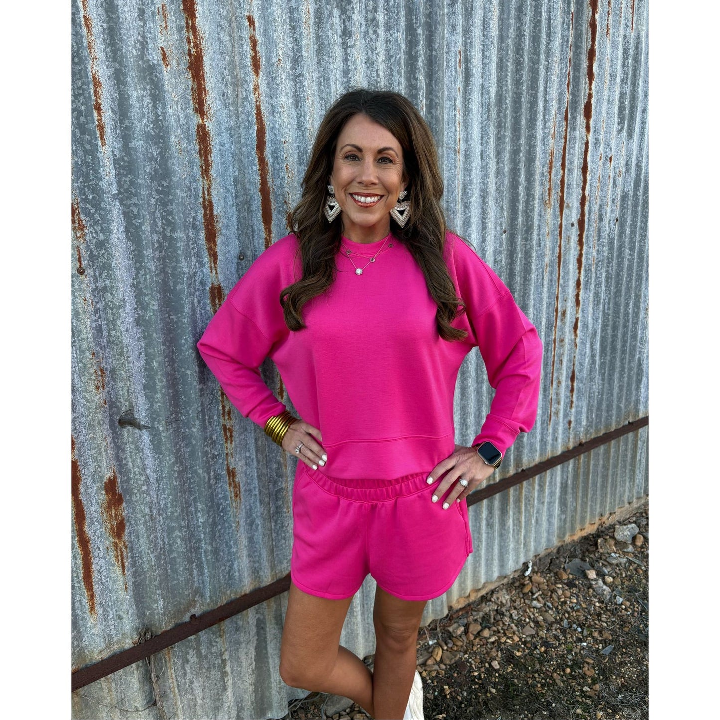 Woman in a bright pink outfit standing against a rusty metal wall.