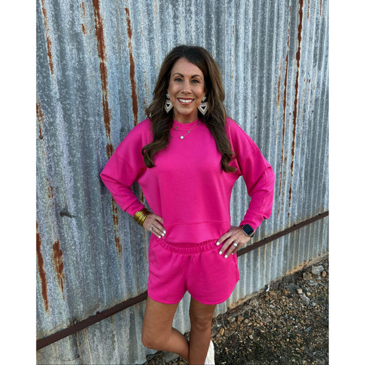 Woman in a bright pink outfit standing against a rusty metal wall.