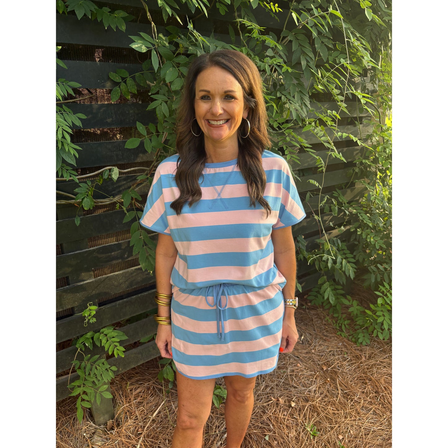 woman wearing a pink and blue striped skort set standing against a black fence. 