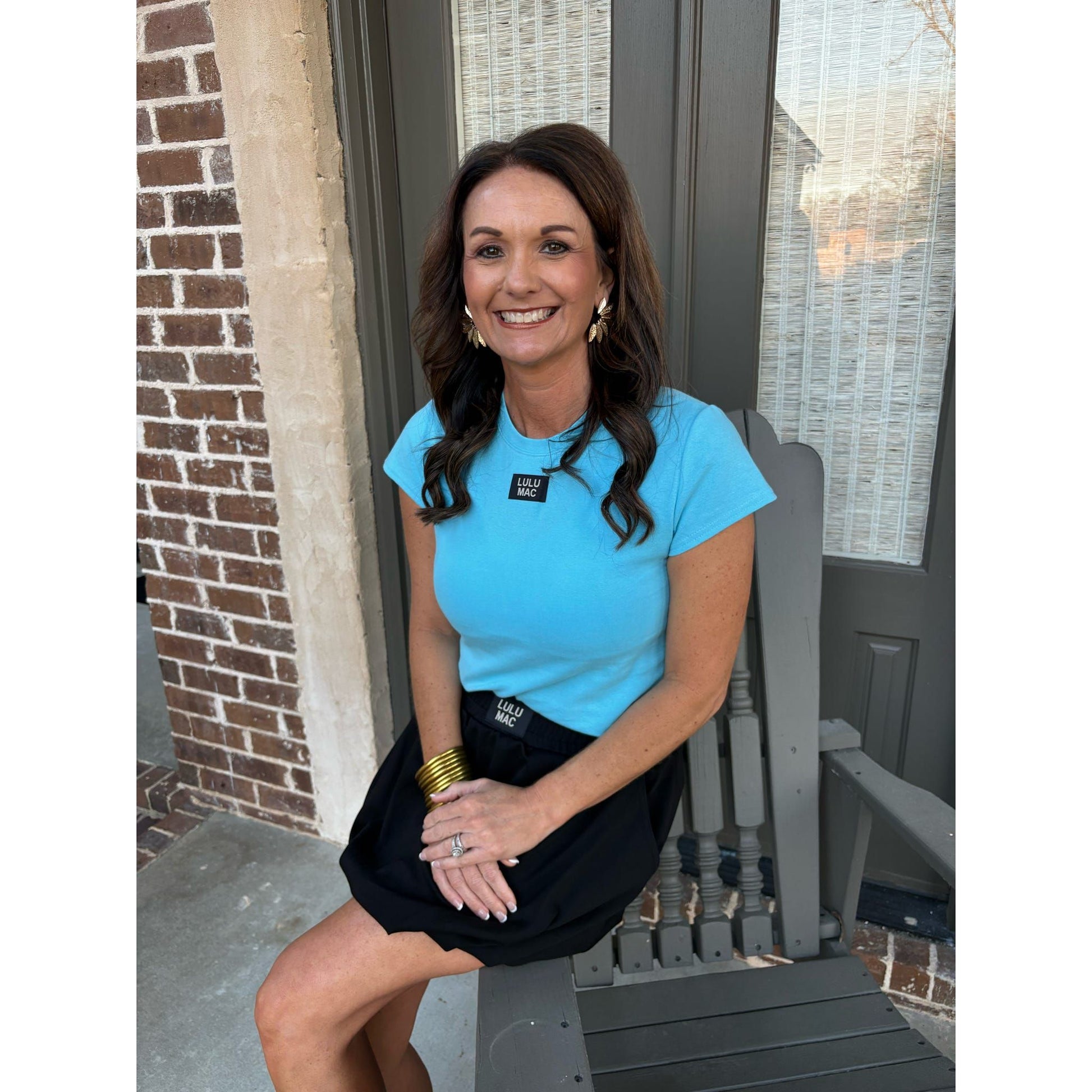 Woman in a blue shirt and black skirt sitting on a chair outside a building.
