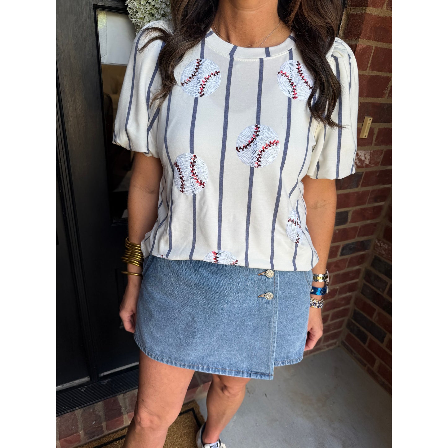 Person wearing a striped shirt and denim skirt sitting on a chair.