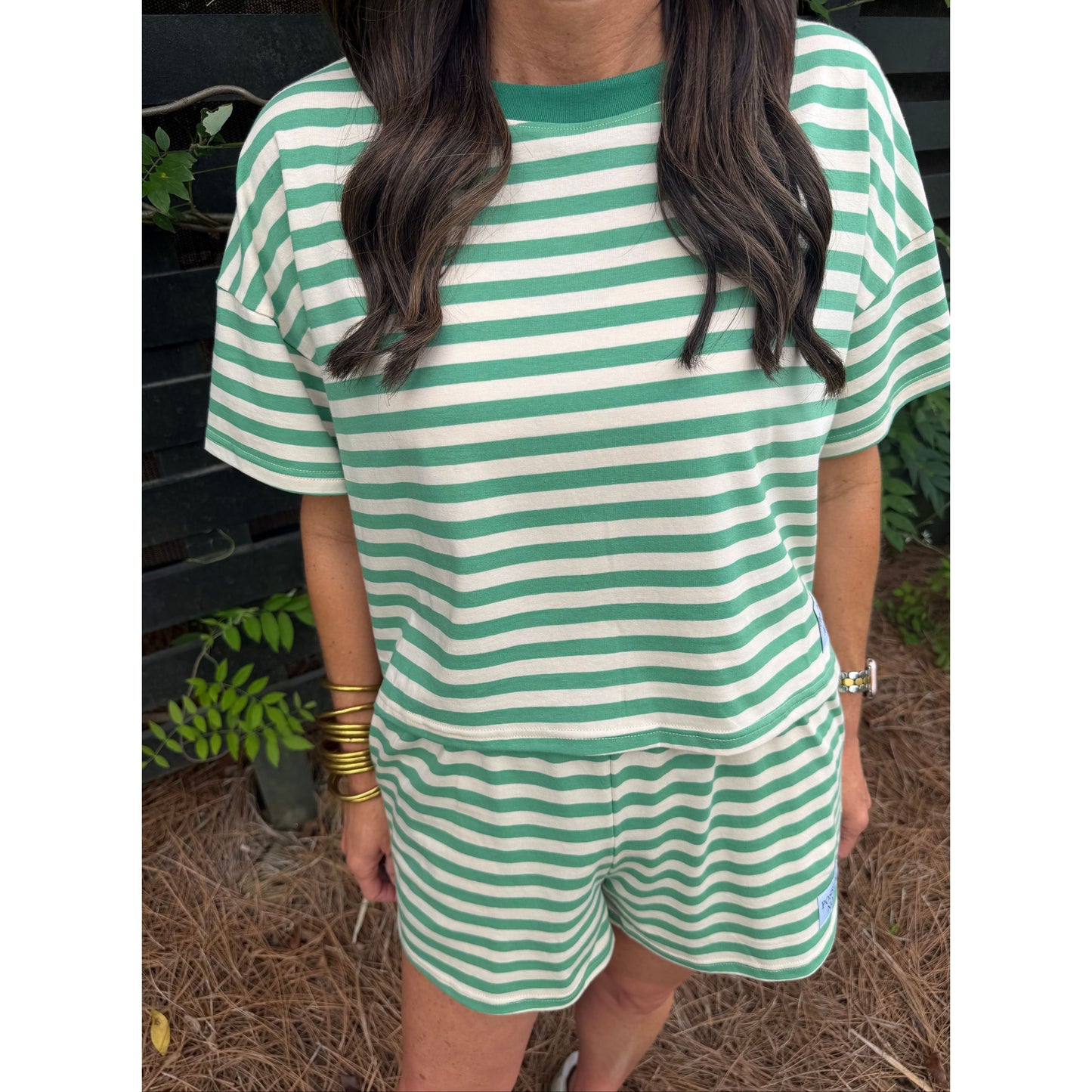 Person wearing a green and white striped dress with plants and dry grass in the background
