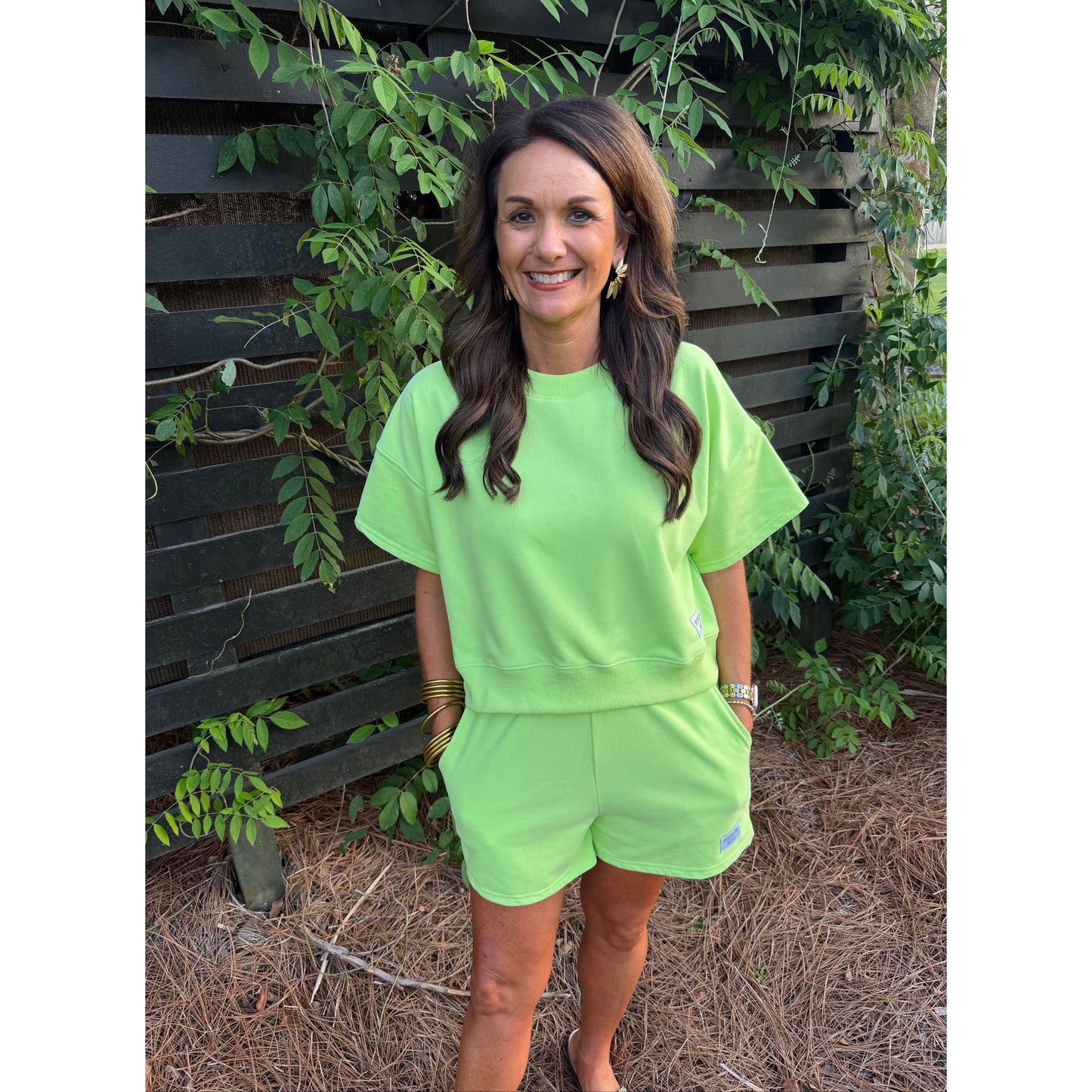 Woman wearing a bright green outfit standing outdoors with greenery in the background