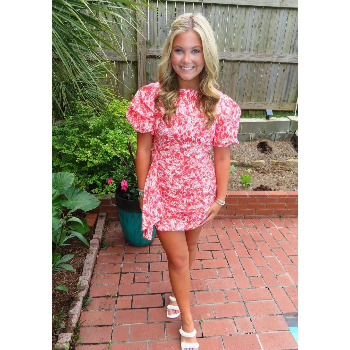 Woman in a red floral dress standing on a brick patio with plants in the background