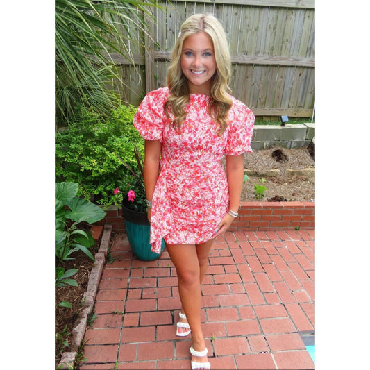 Woman in a red floral dress standing on a brick patio with plants in the background